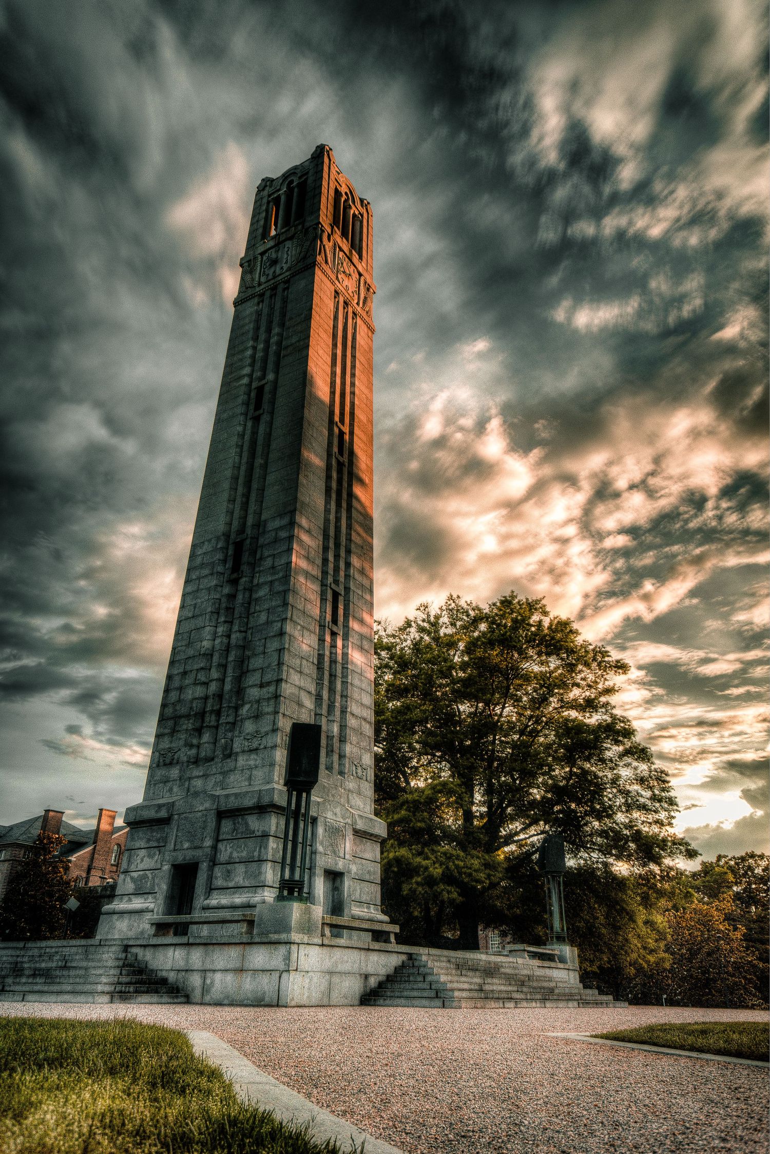 Tall historic belltower monument at sunset with dramatic cloudy sky and autumn trees in background.