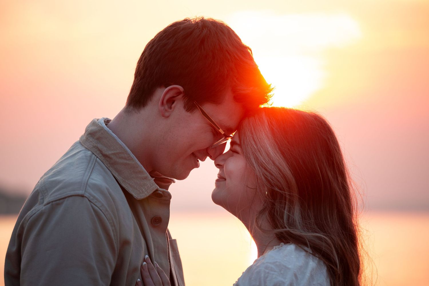 Silhouetted couple embraces romantically against vibrant orange sunset sky in tender moment.