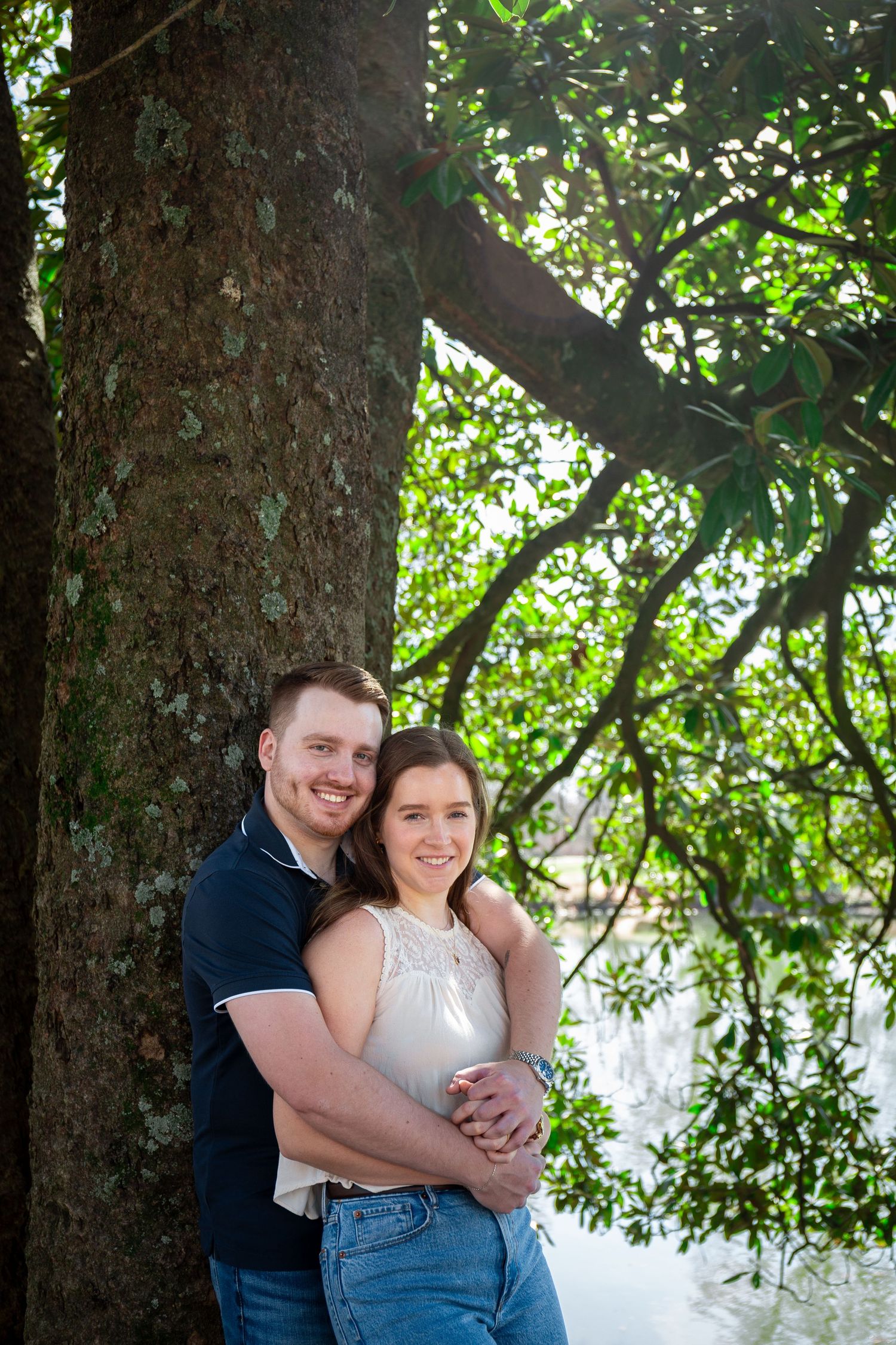 A couple shares a loving embrace under a large tree during an outdoor photo session.