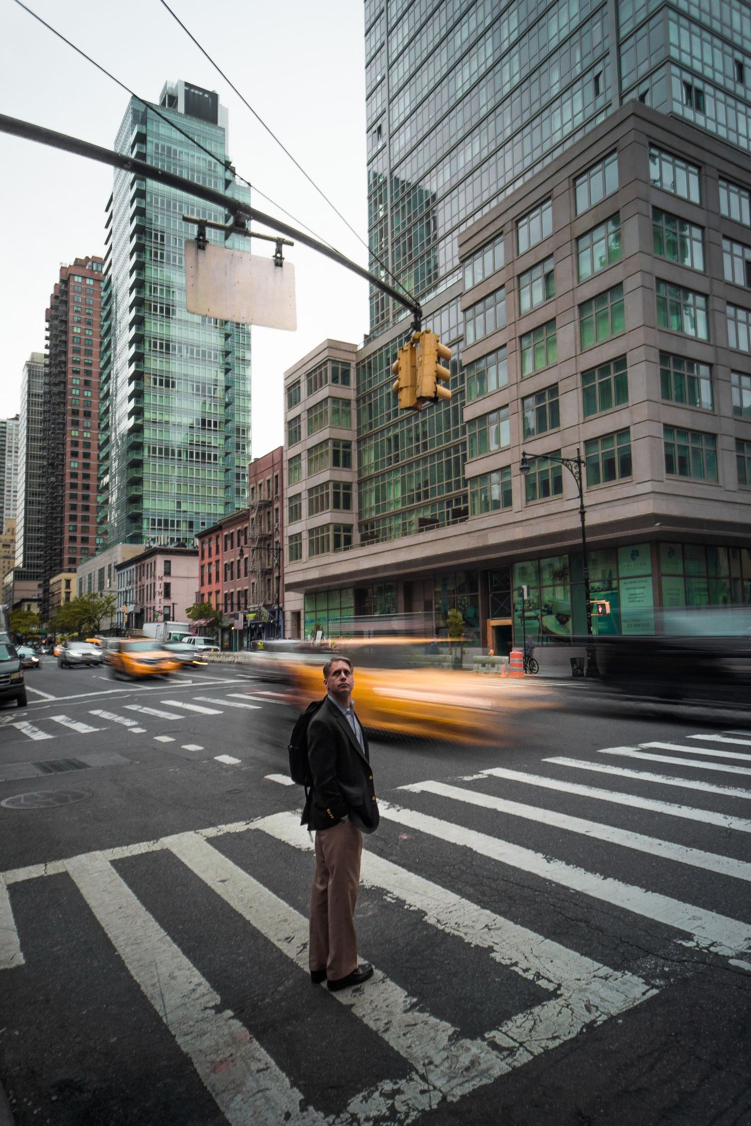 Man standing on crosswalk in busy New York City intersection with yellow taxis and glass skyscrapers.