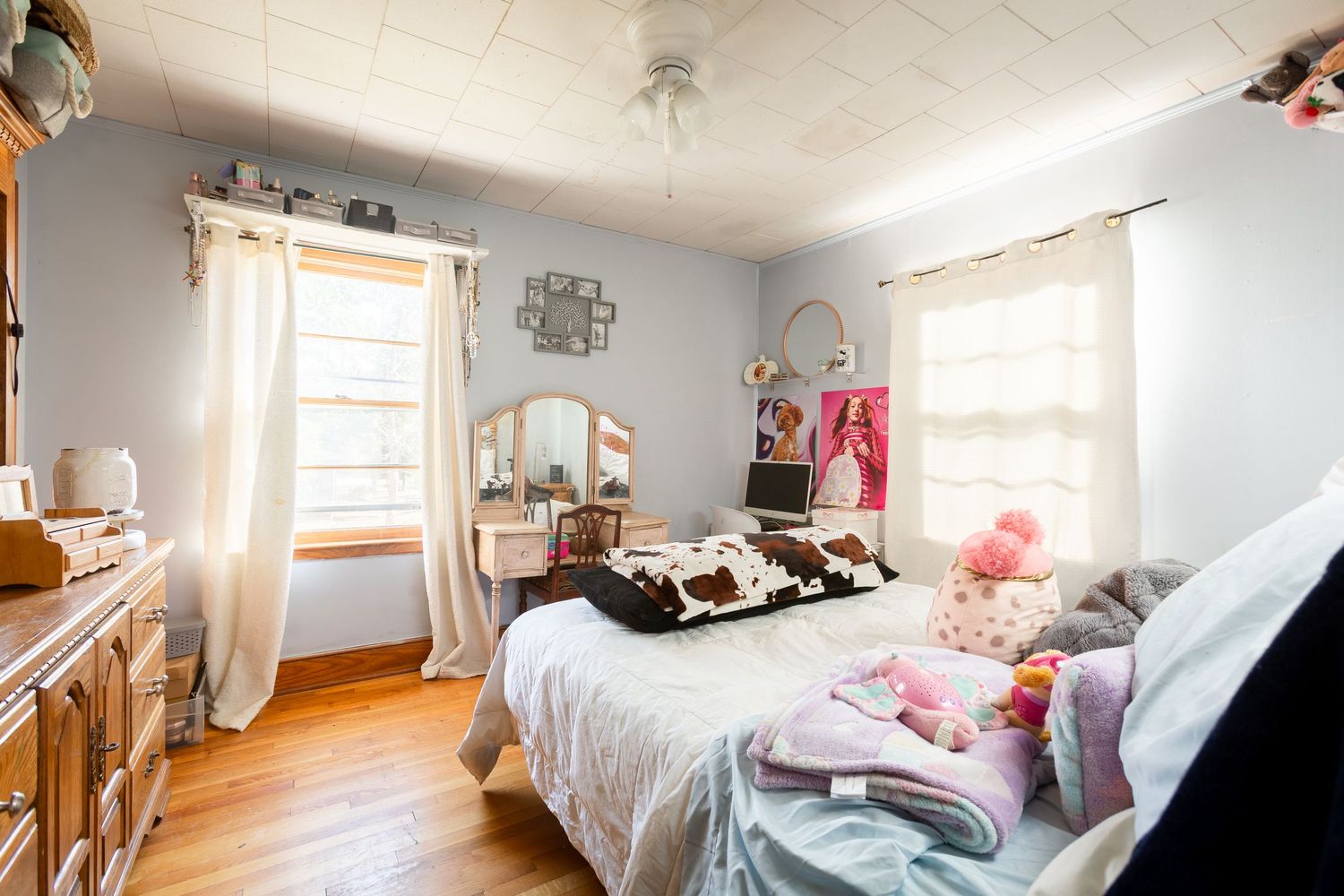 Cozy bedroom interior with white bedding, natural light streaming through windows, and rustic wooden furniture.