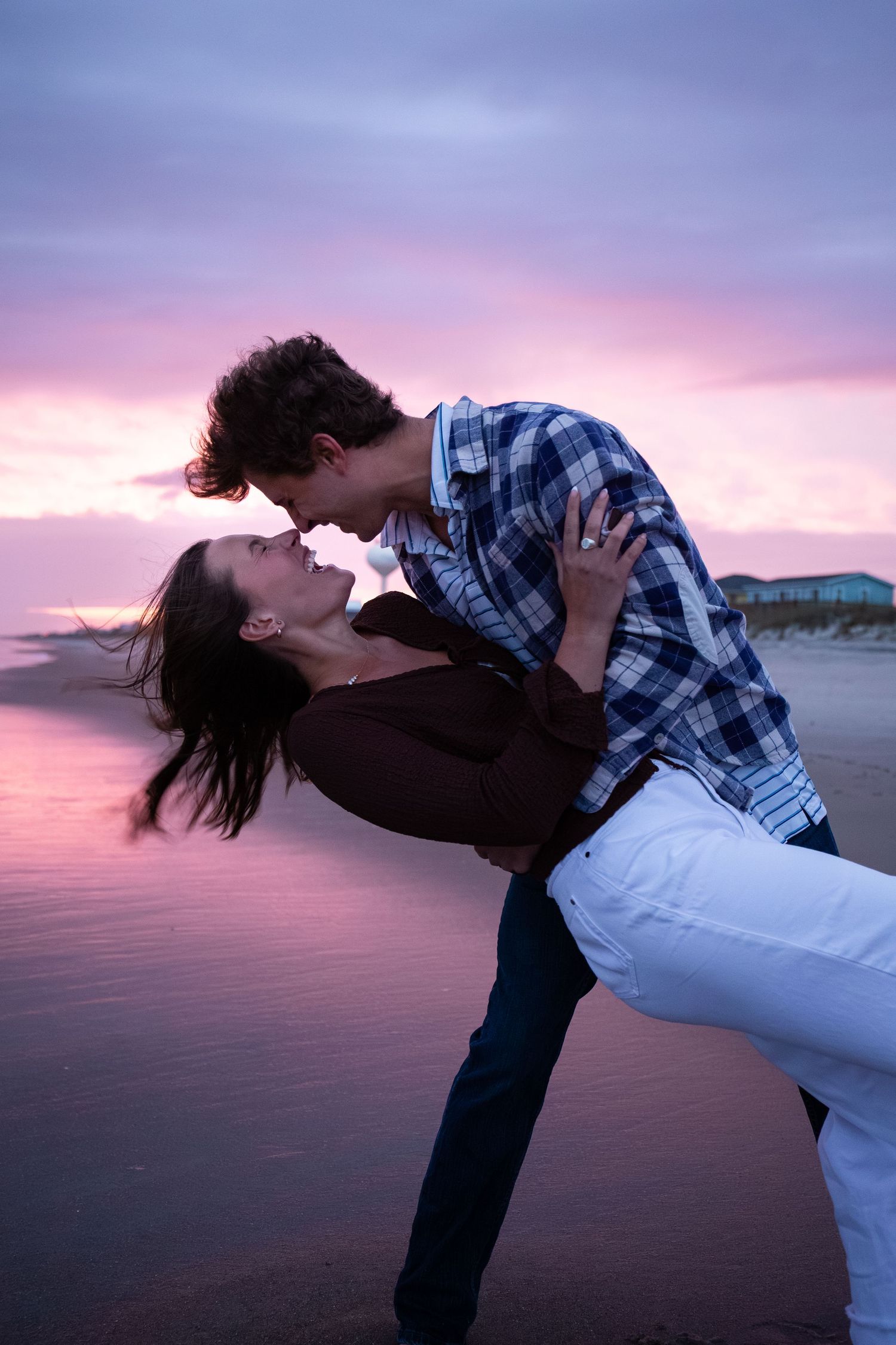 Romantic couple embracing during sunset by a lake with pink and purple sky.