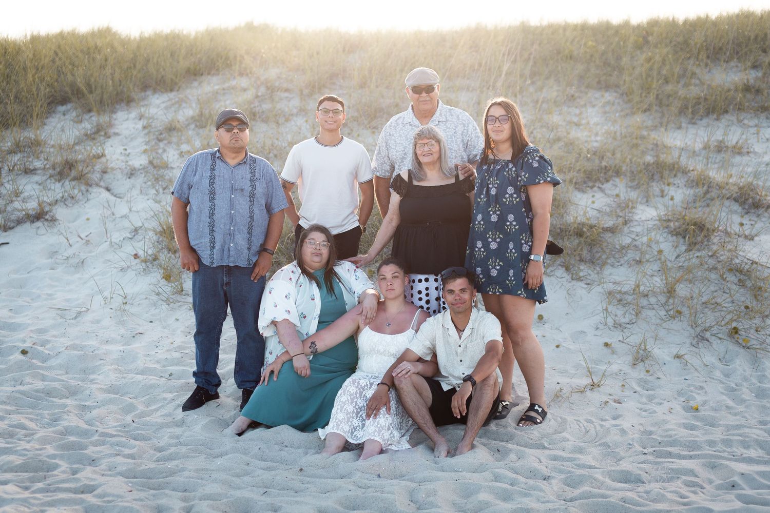 A group poses casually together on sand dunes during sunset with warm lighting.