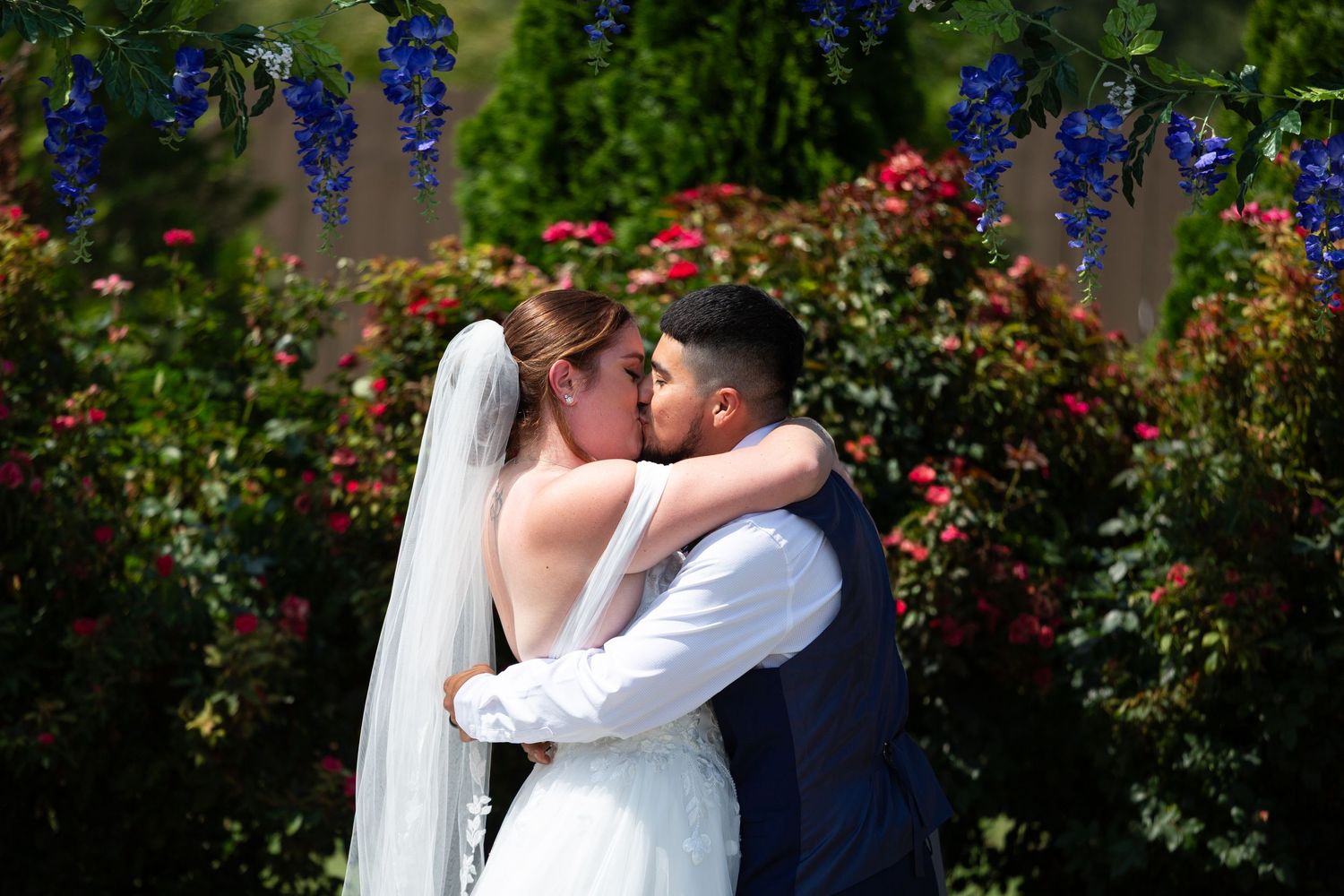 Romantic couple embraces in a garden setting with vibrant purple flowers and greenery.