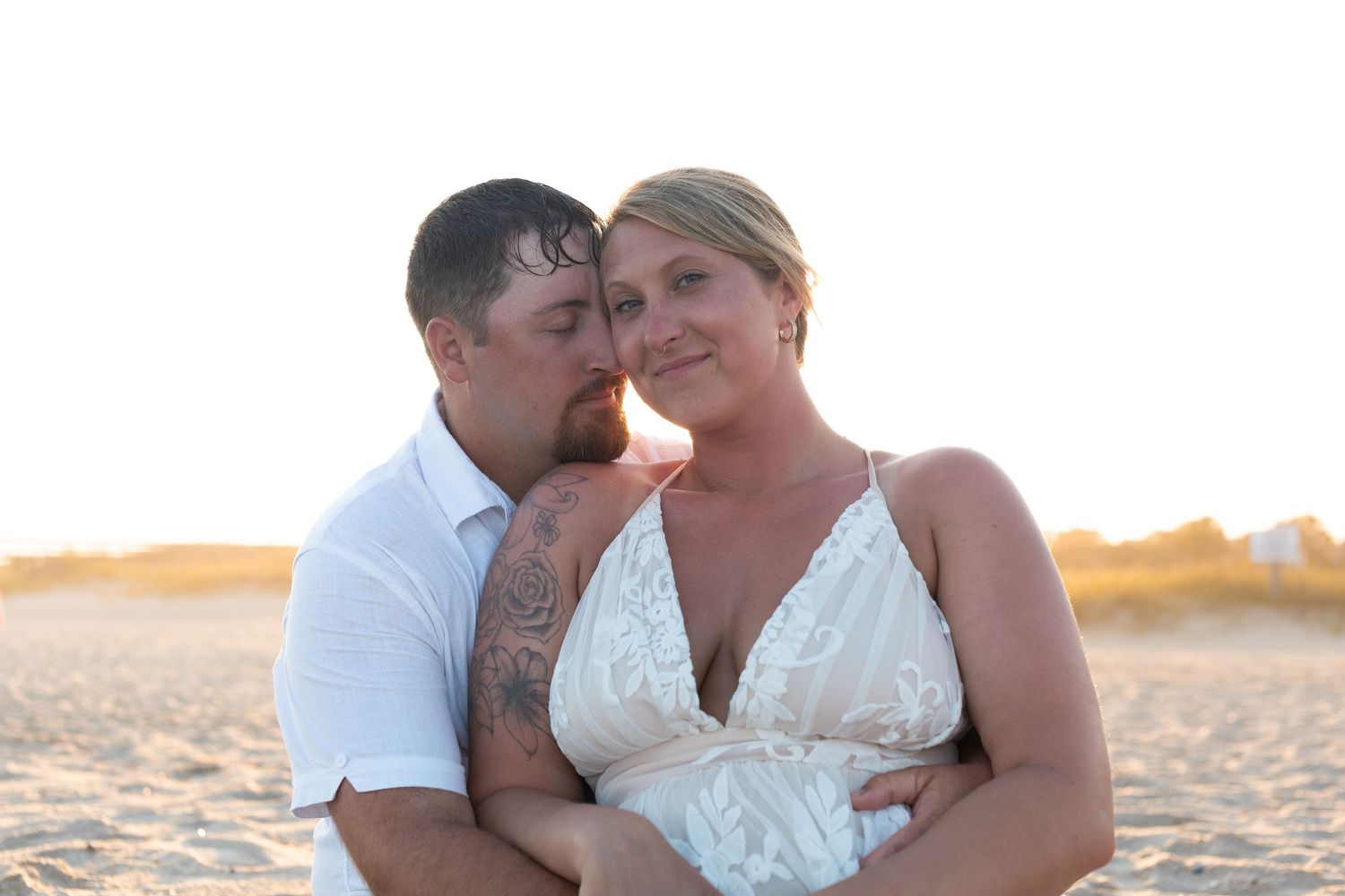 A couple shares an intimate moment on a sandy beach during sunset.