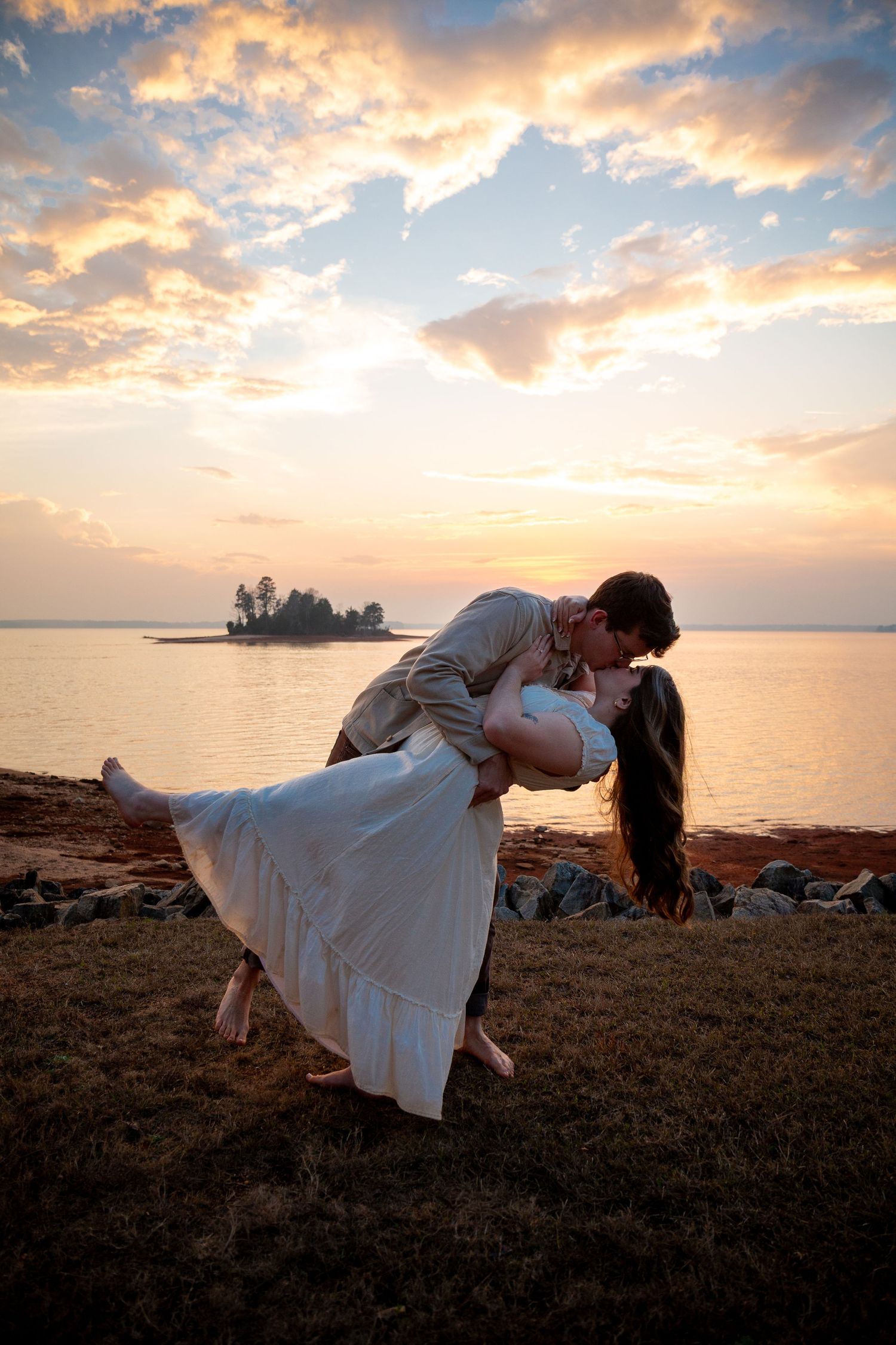 A romantic sunset silhouette of a couple in a dip pose against a dramatic orange sky over the ocean.