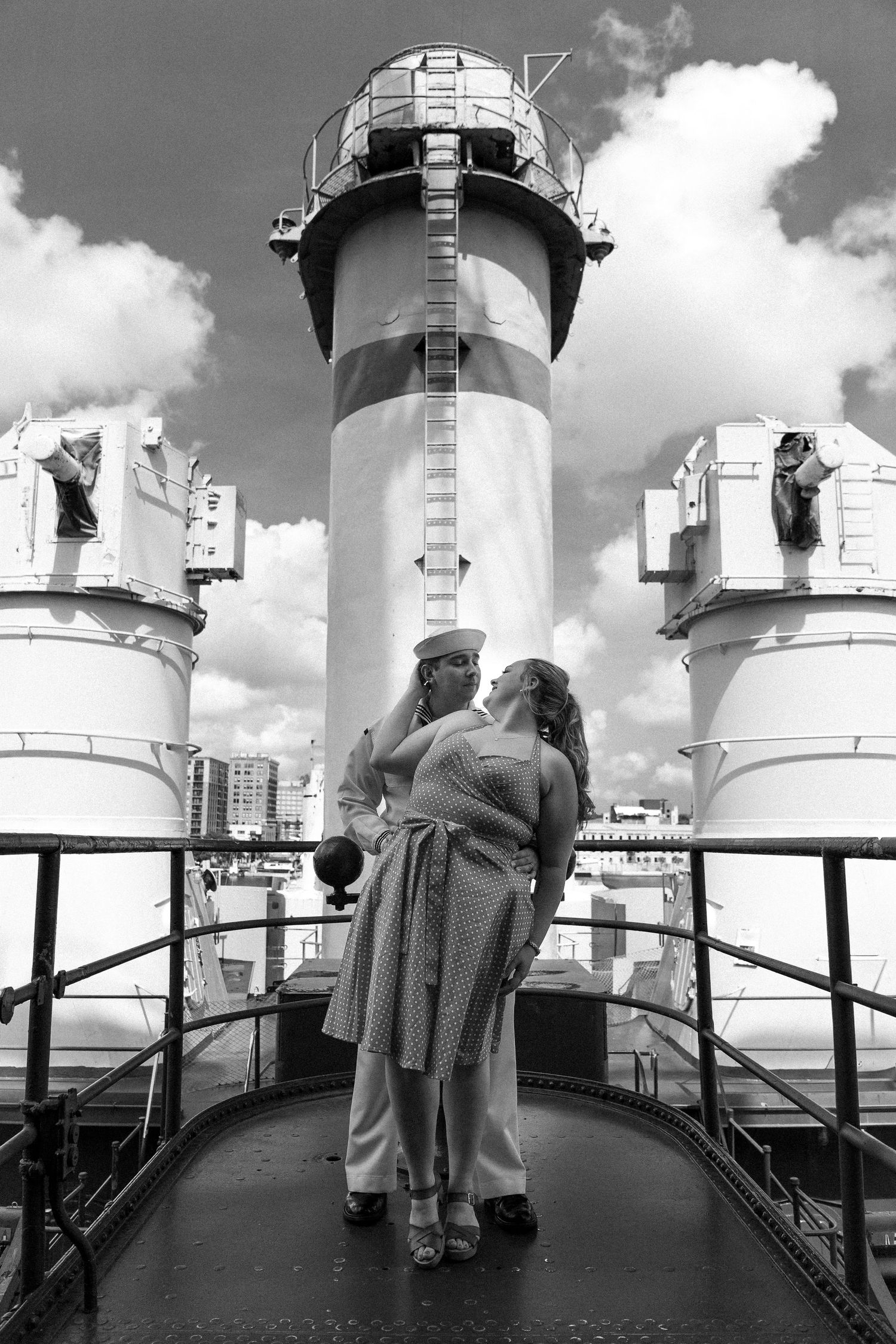 A black and white triptych shows people looking out over a railing at lighthouse towers on a cloudy day.
