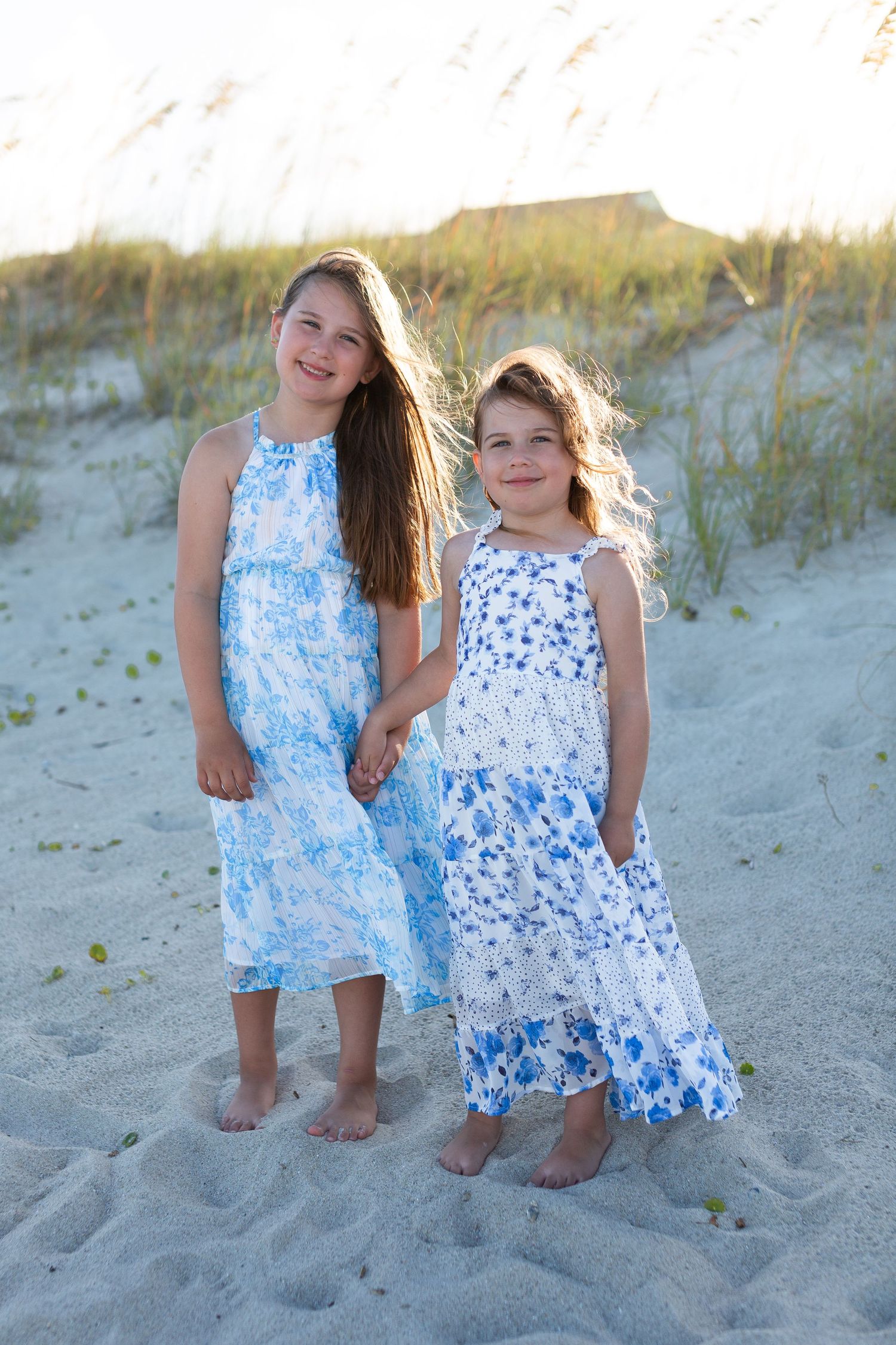 Children in blue and white floral dresses playing on sandy beach.
