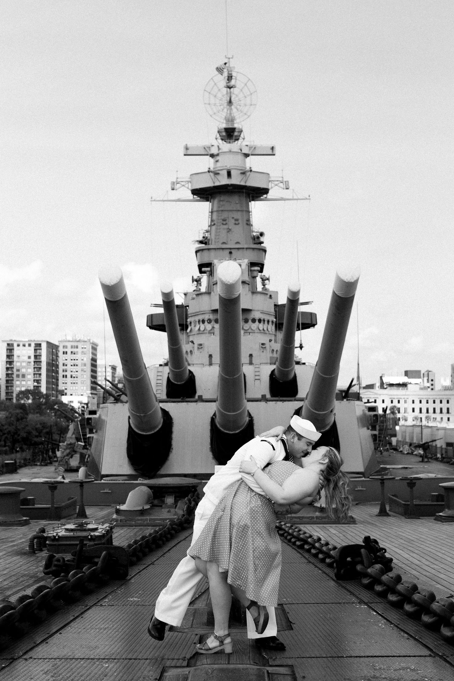 A classic black and white romantic pose on the deck of a battleship with large guns in the background.
