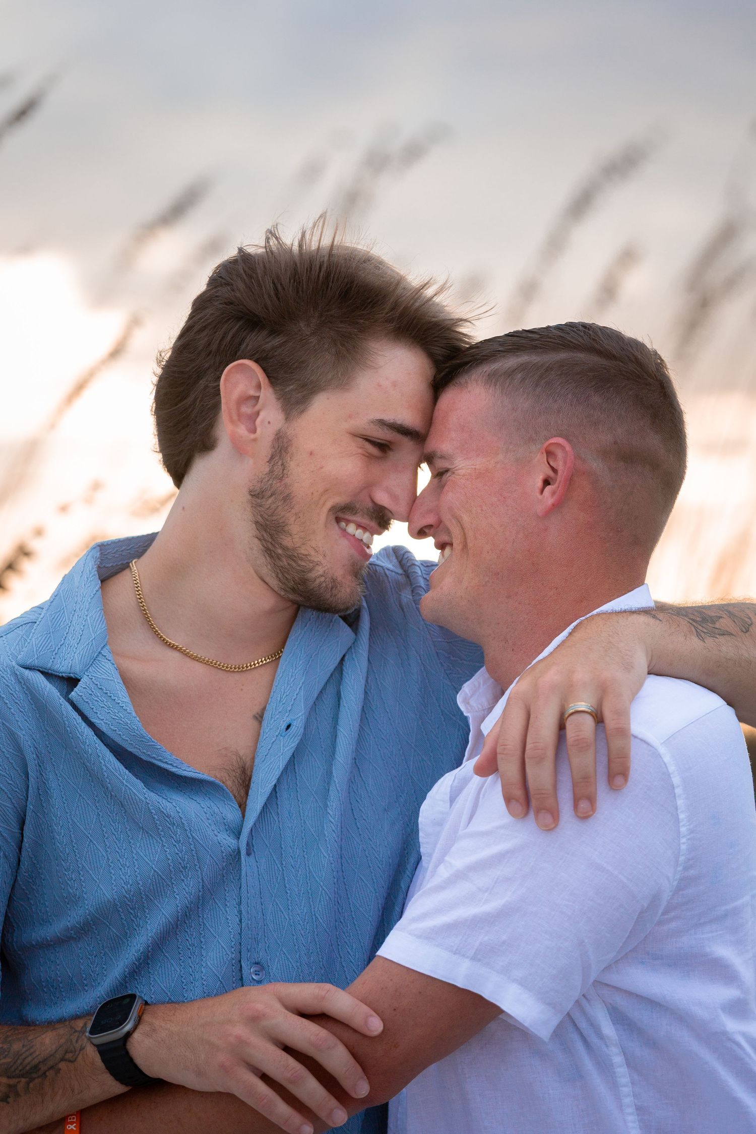 A couple shares an intimate moment against a sunset backdrop with sea grass in the foreground.