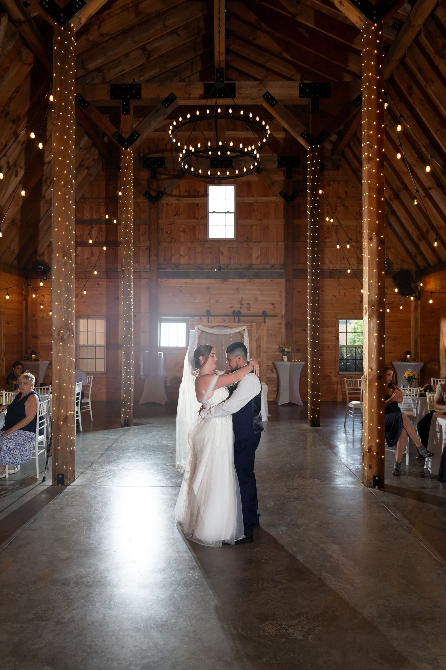A series of photos showing a rustic barn wedding venue interior decorated with string lights and wooden beams.