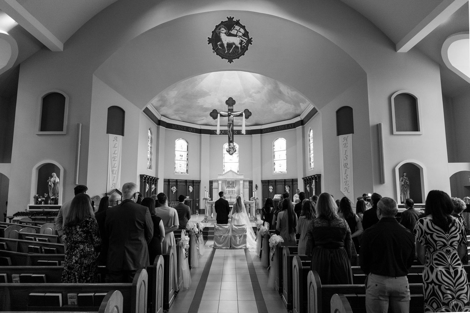 Black and white photo of a wedding ceremony inside a beautiful church with guests seated in pews.