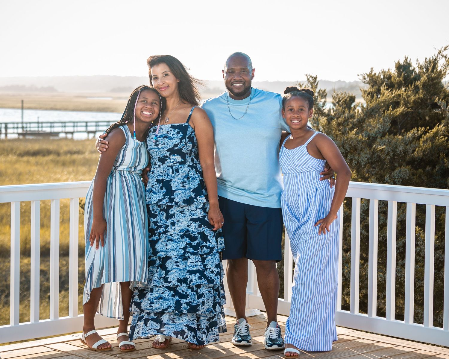 Family group wearing coordinated blue and white outfits poses together on wooden deck.