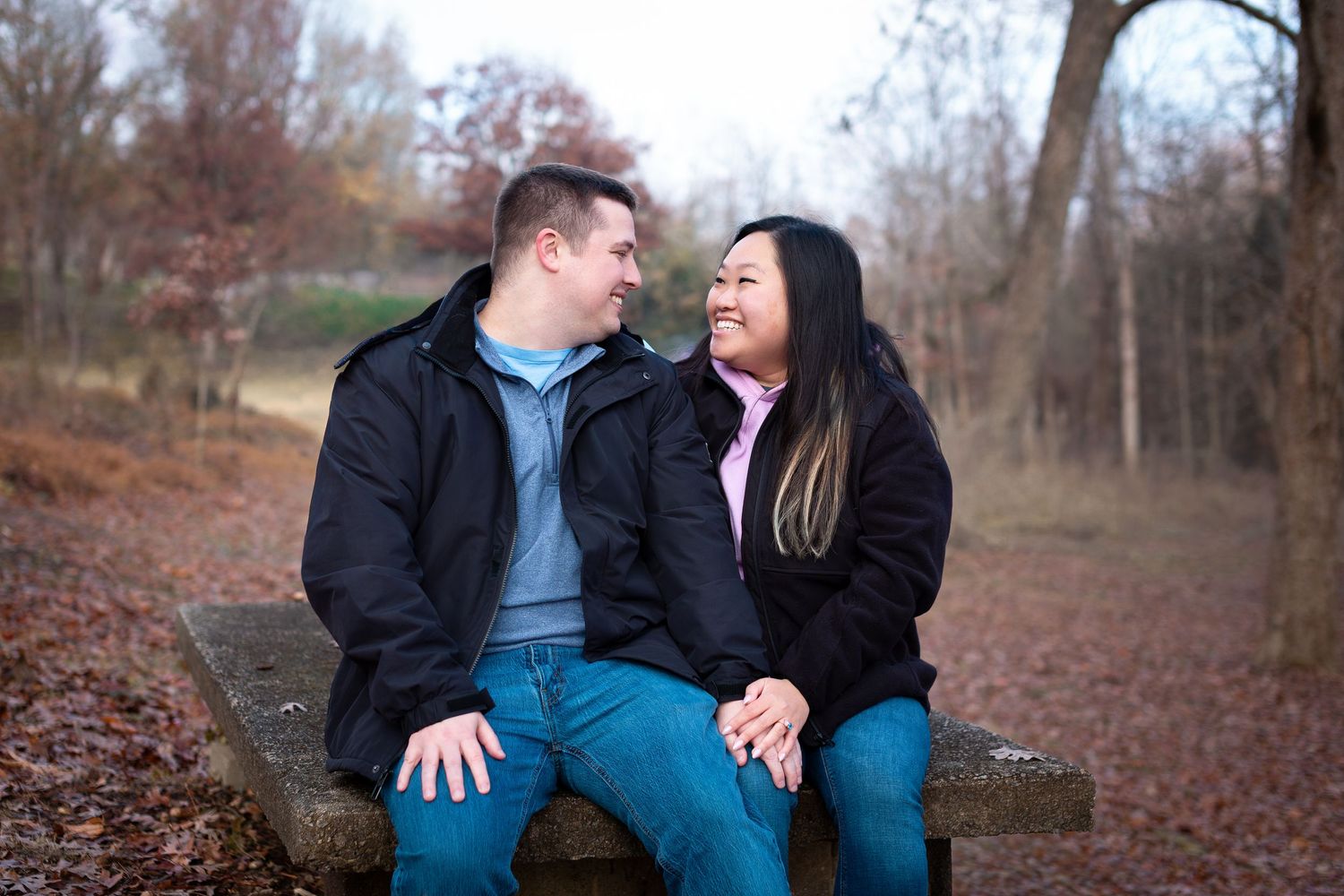 Couple sitting together on fallen autumn leaves in a wooded park during a casual outdoor photoshoot.