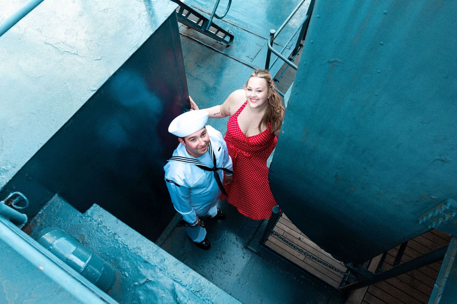 A person wearing a red shirt and blue jeans stands near a dark wall in a dimly lit industrial setting.