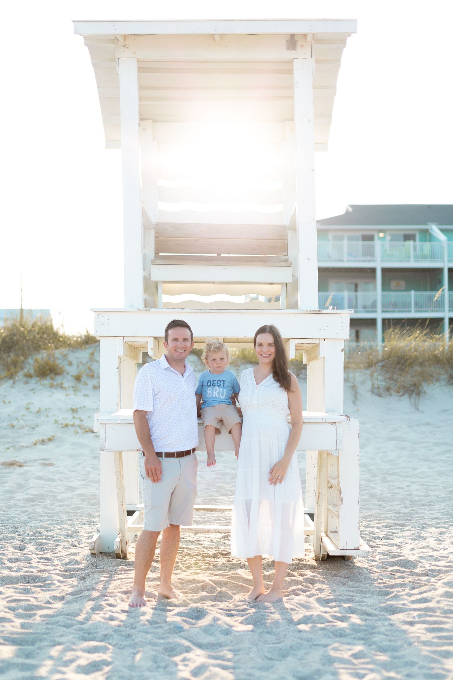 Family portrait session with feet in white sand at beach under gazebo during sunset.