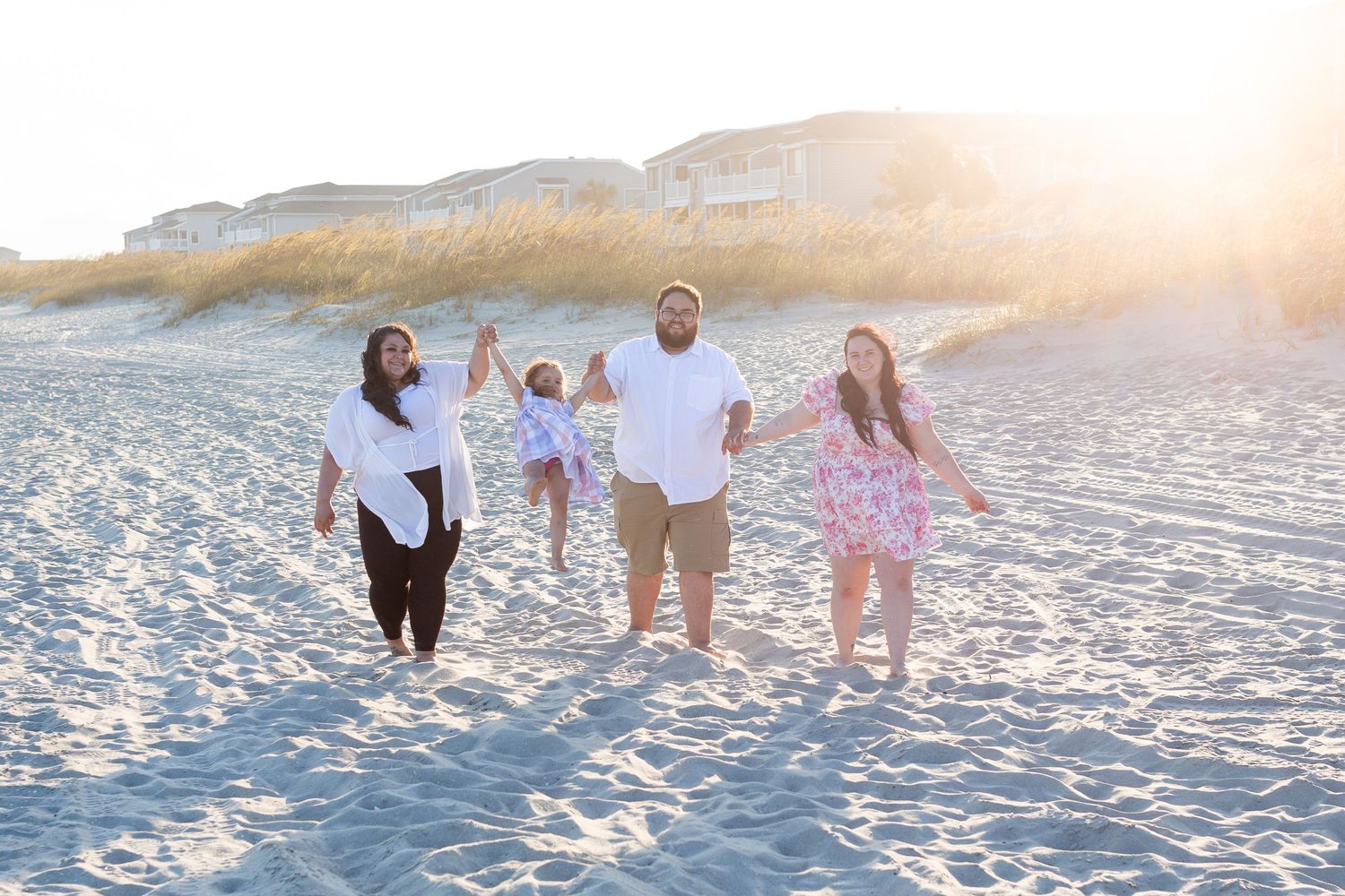 A family walking together on a white sandy beach at sunset creates a serene silhouette against the golden sky.