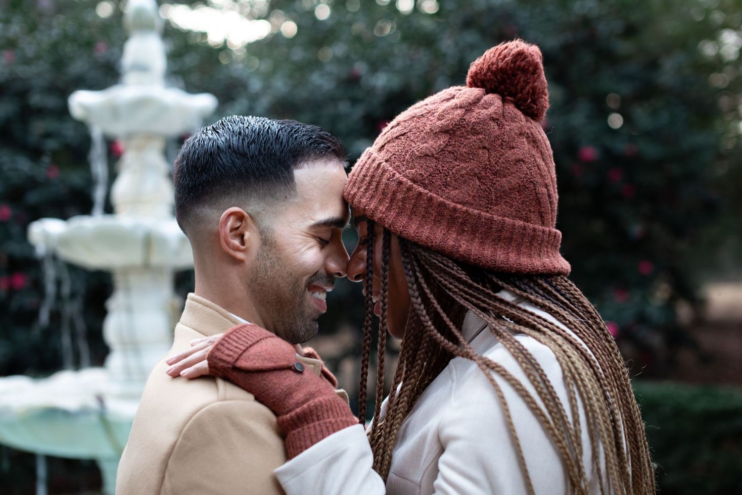 A couple in brown winter hats share an intimate moment outdoors during autumn.