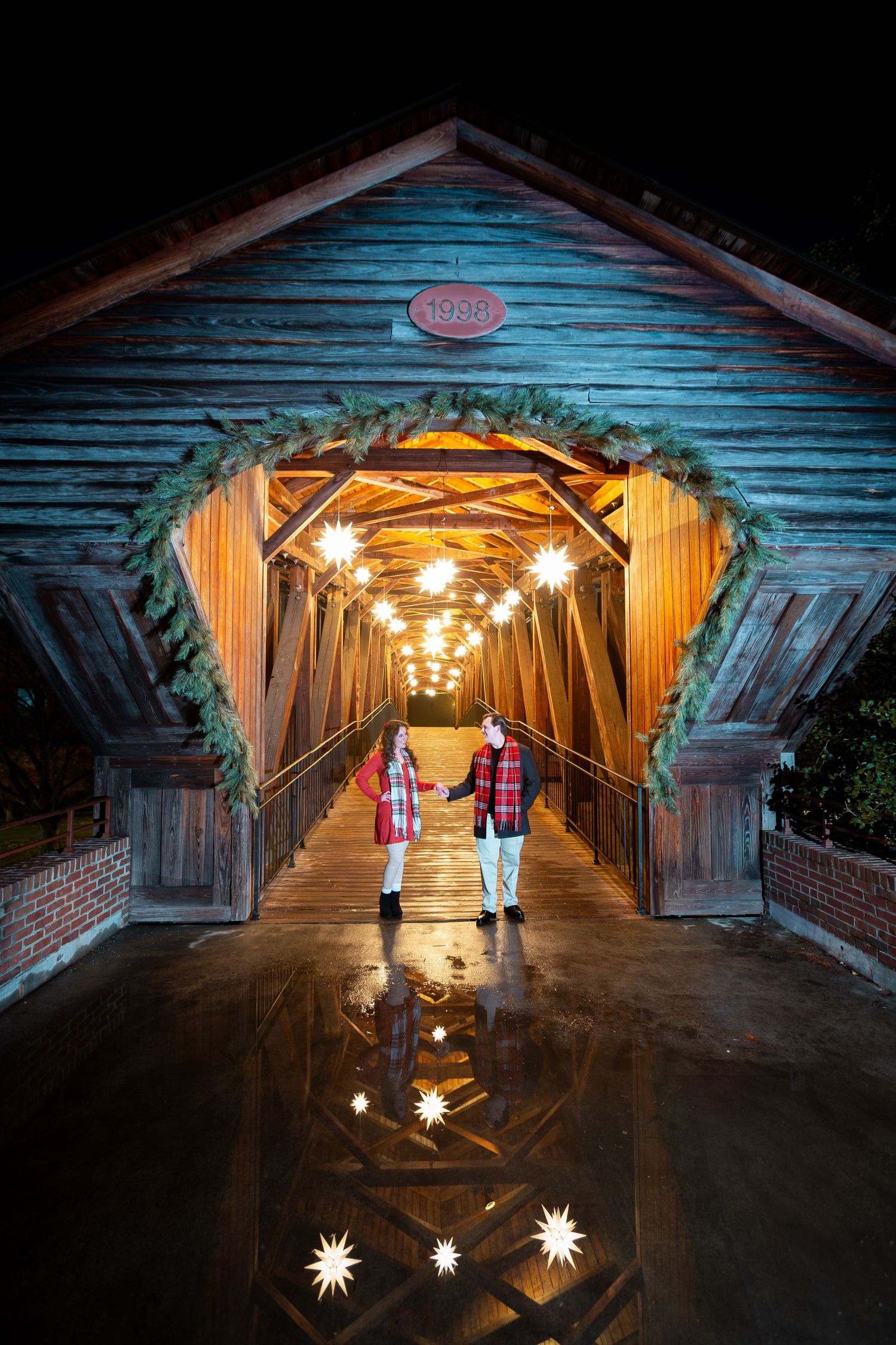 A rustic covered bridge illuminated at night with glowing star-shaped lanterns creating a magical tunnel effect.