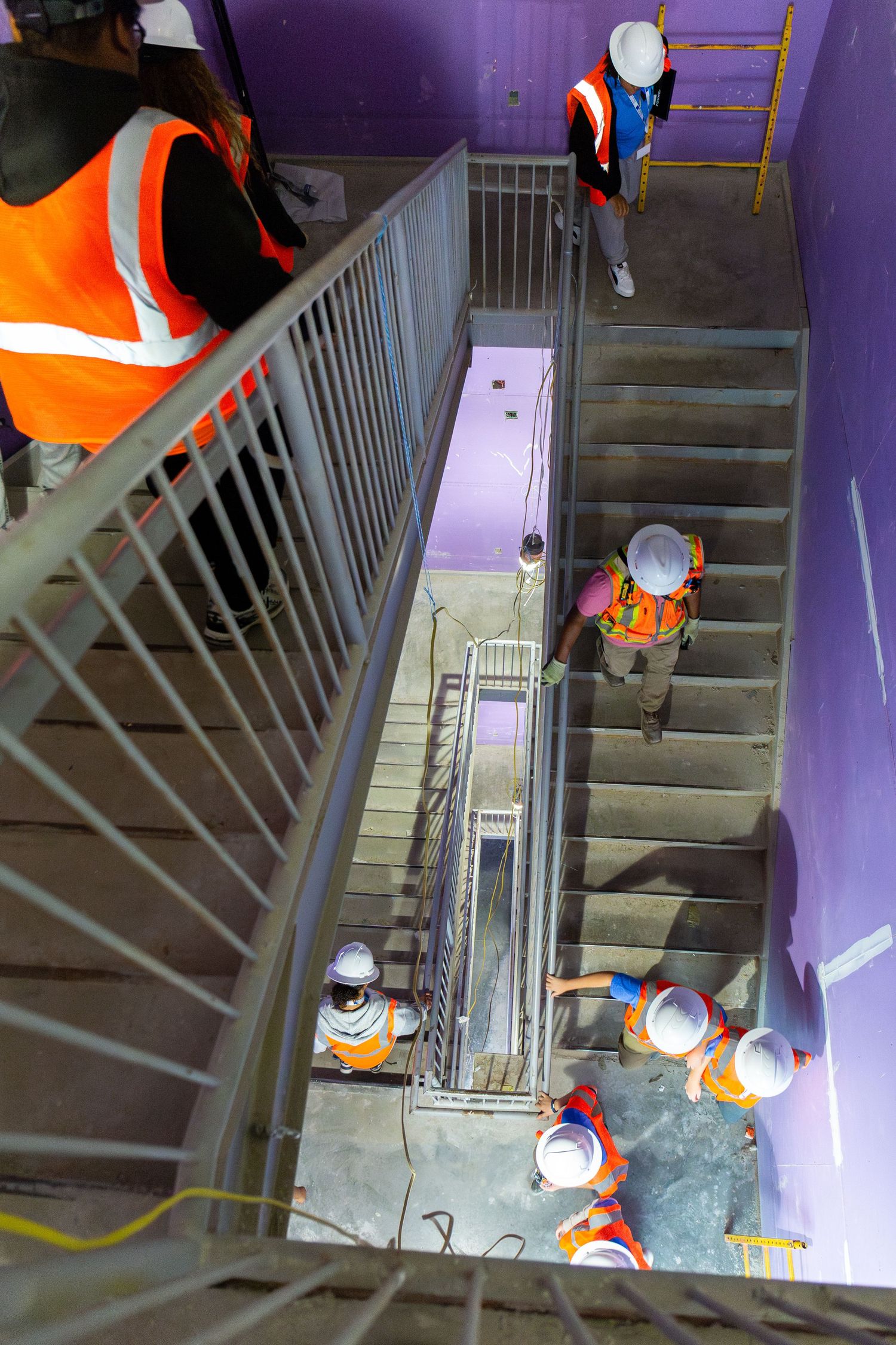 Workers in orange safety vests inspecting a purple-walled stairwell during construction or maintenance.