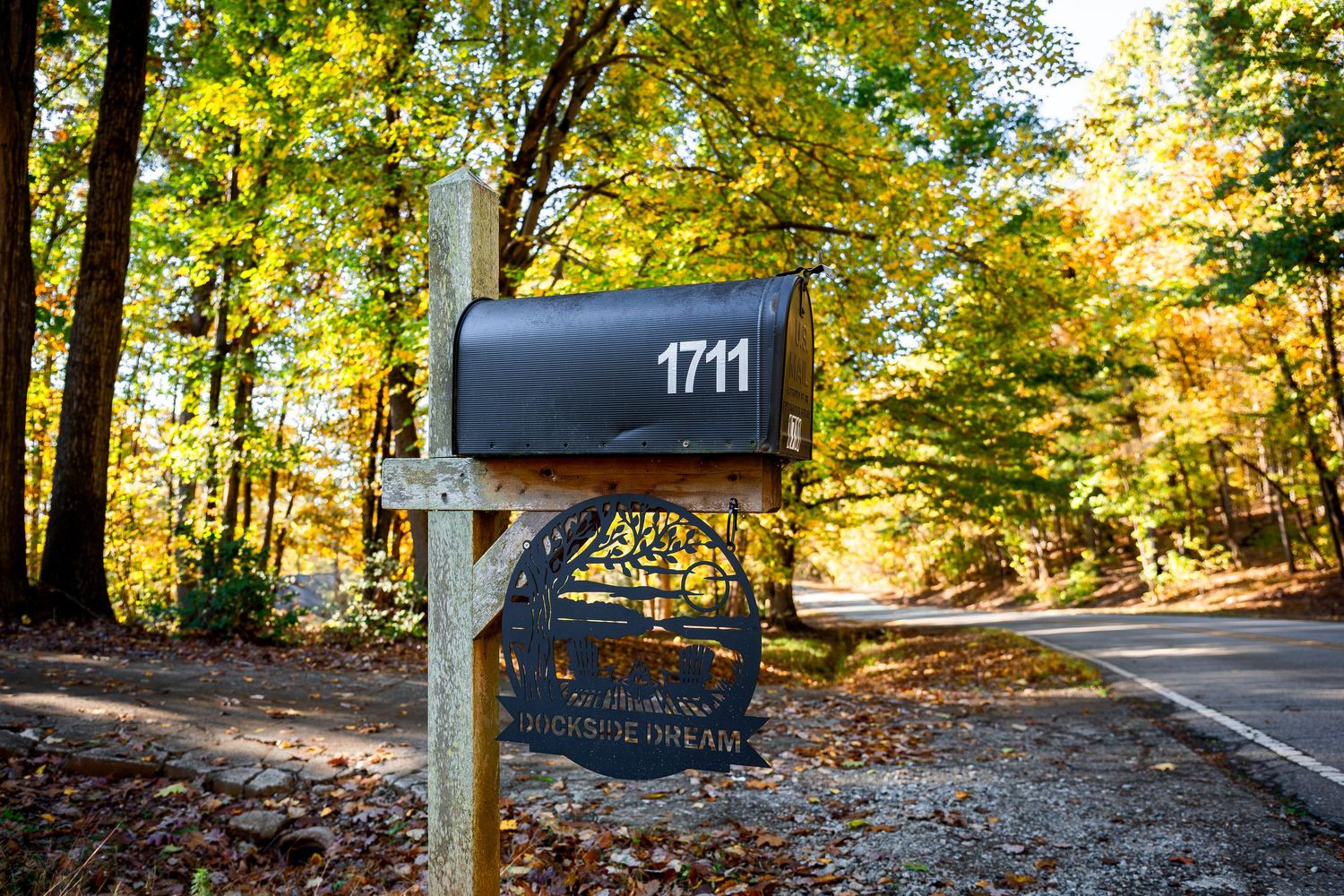 A rustic mailbox numbered 1714 stands along a tree-lined autumn road with golden foliage.