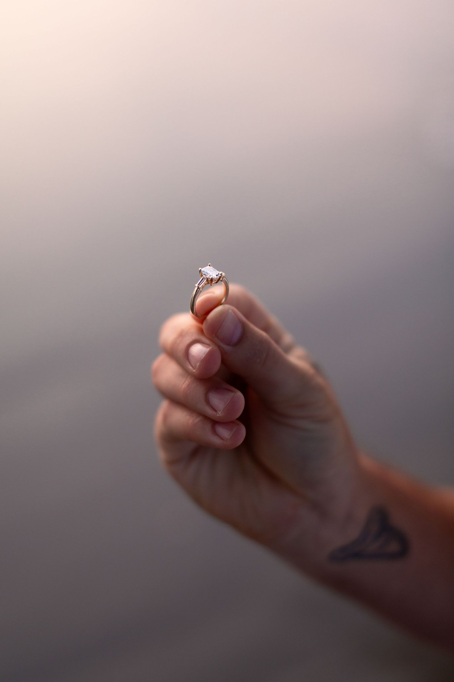 Close-up shot of hands holding an engagement ring against a blurred background.