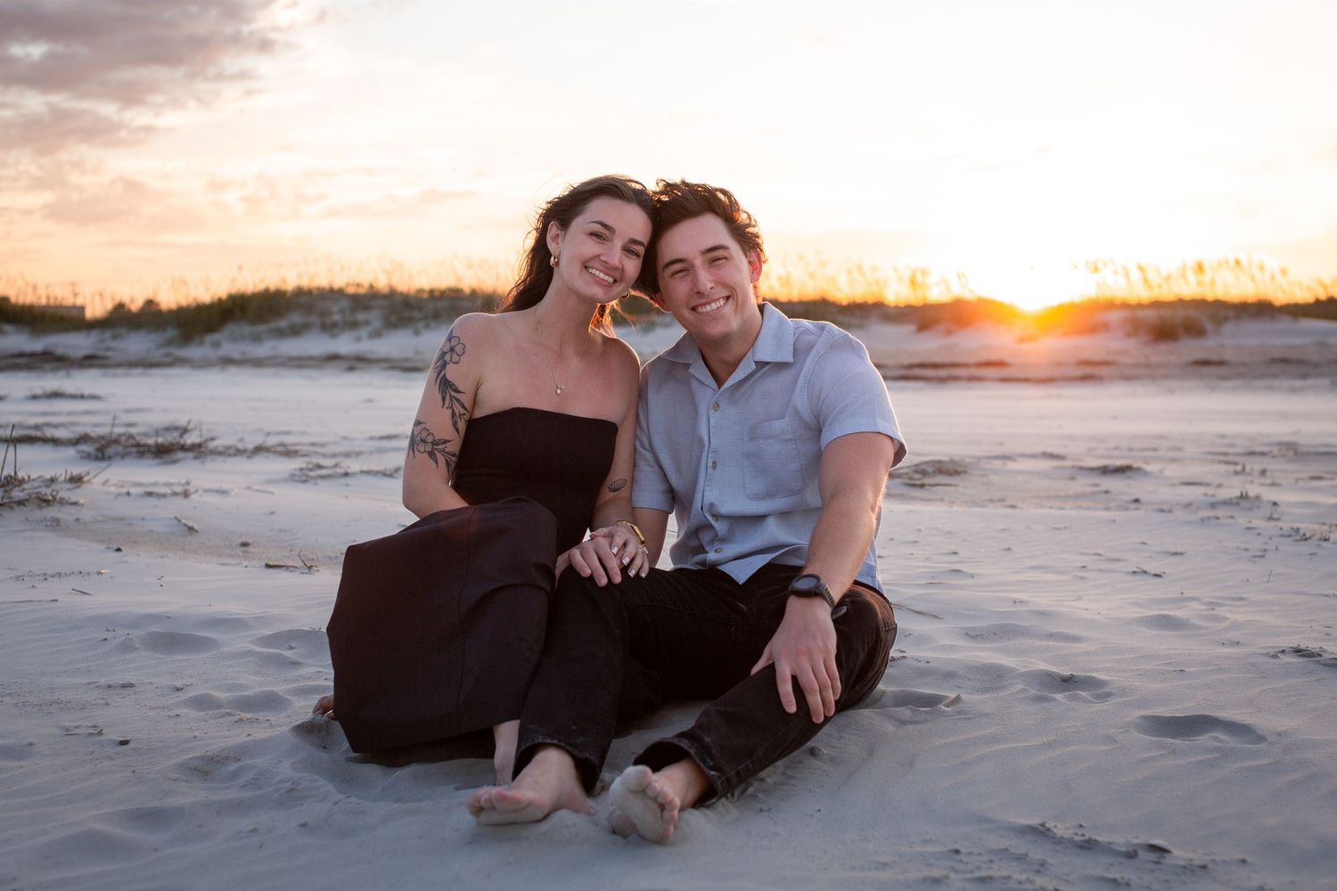 A couple sitting together on a sandy beach at sunset with warm golden lighting.