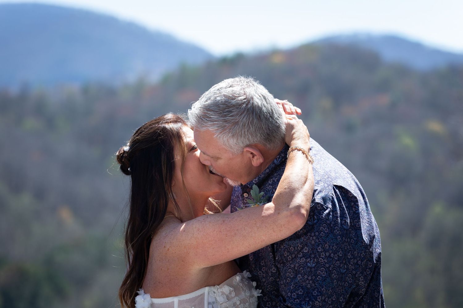 A couple shares a romantic moment in front of a scenic mountain landscape during their wedding photoshoot.