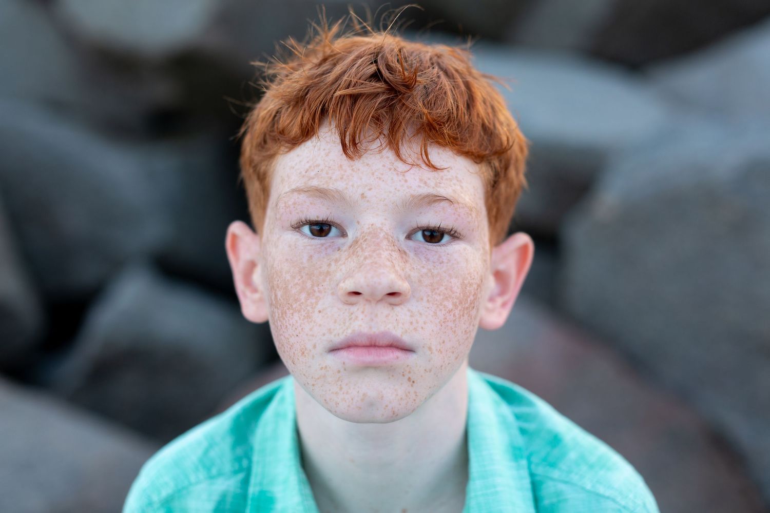 Close up portrait of young child with freckles wearing turquoise shirt against dark background.