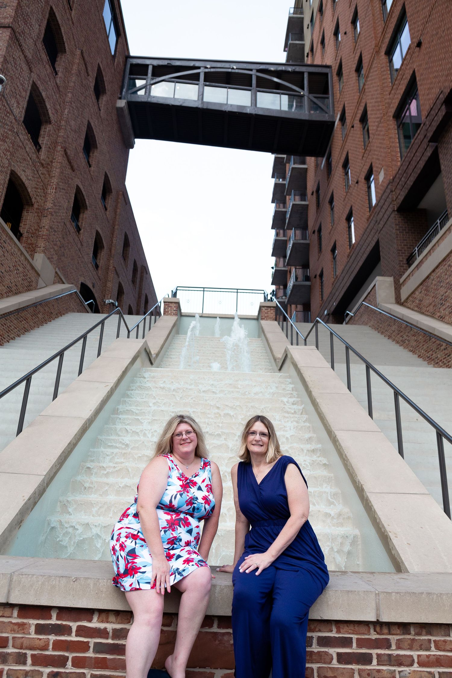 Two people pose on brick steps with industrial architecture in background.