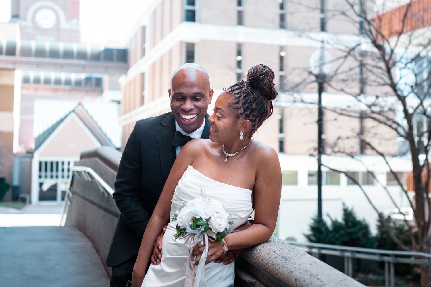 A couple in wedding attire shares an intimate moment outdoors near an urban building.