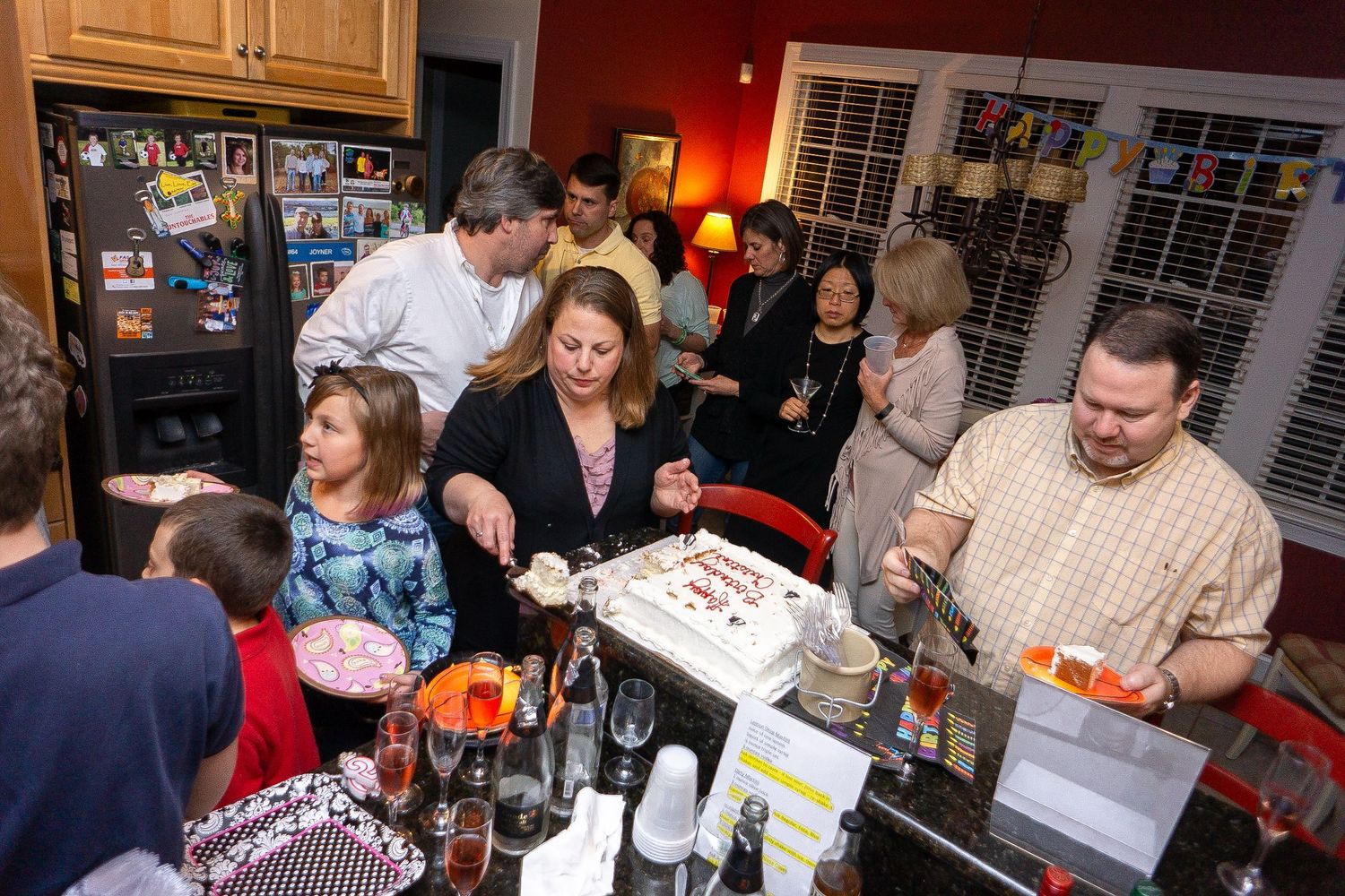 Group of people gathered at a social event mingling and looking at papers in a warmly lit room.