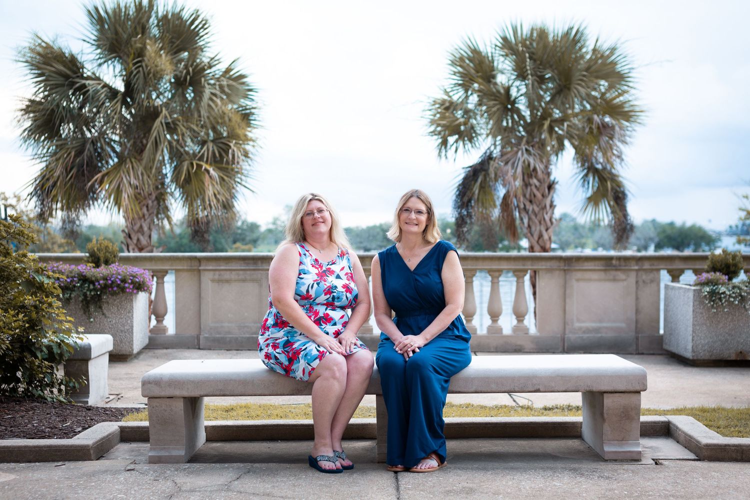 Casual family portraits on stone bench with palm trees at beachfront location.