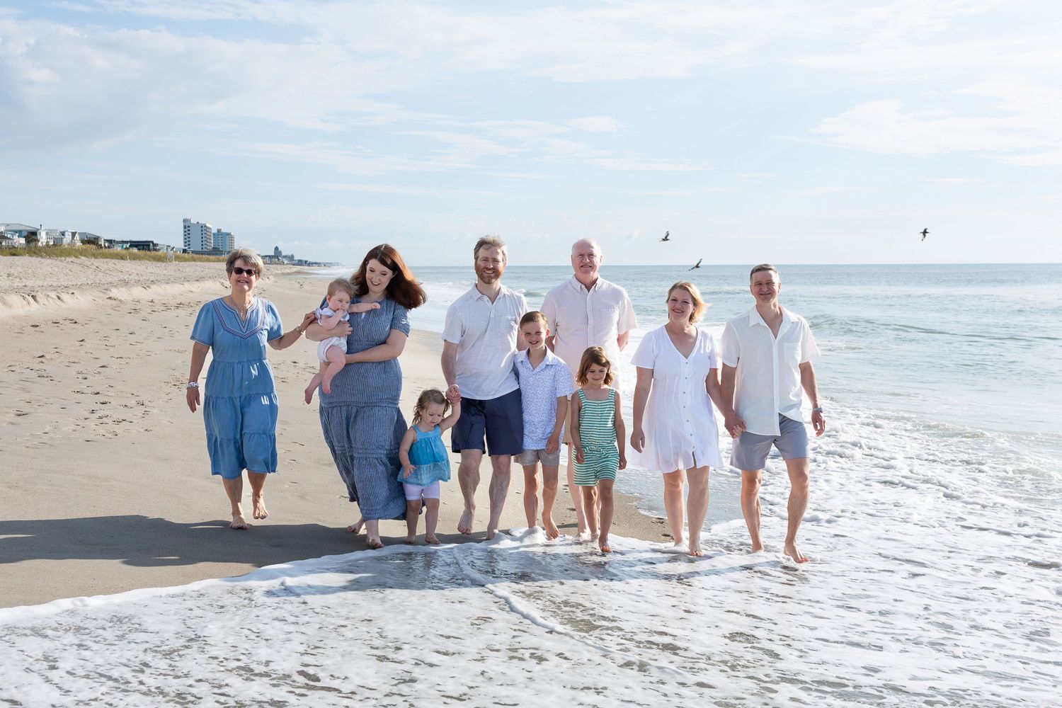 A joyful group walks together along the ocean's edge on a sunny beach day.