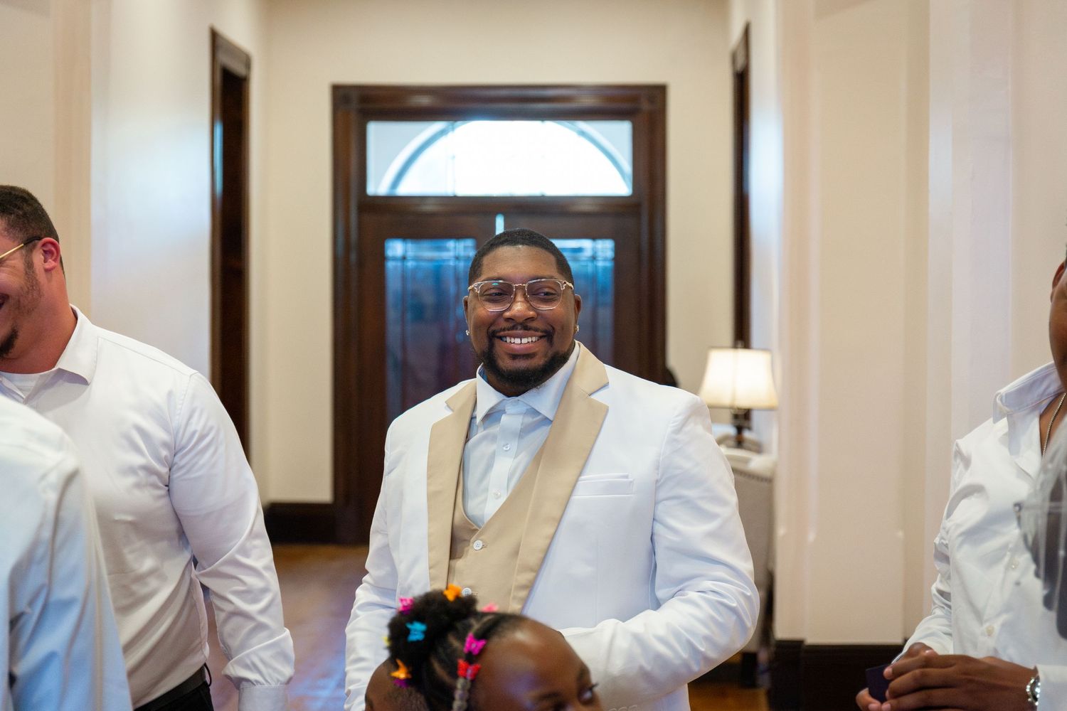 Smiling groom in white suit with gold tie at wedding venue entrance.