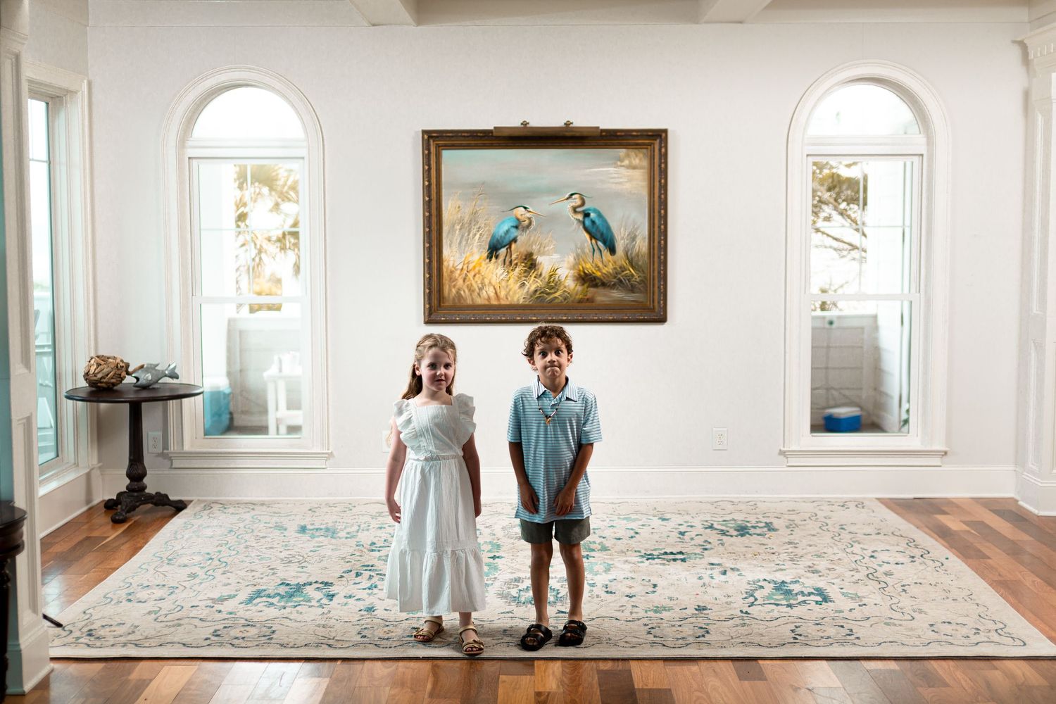 A bright white gallery space with arched windows displays framed artwork and a figure standing near the wall.