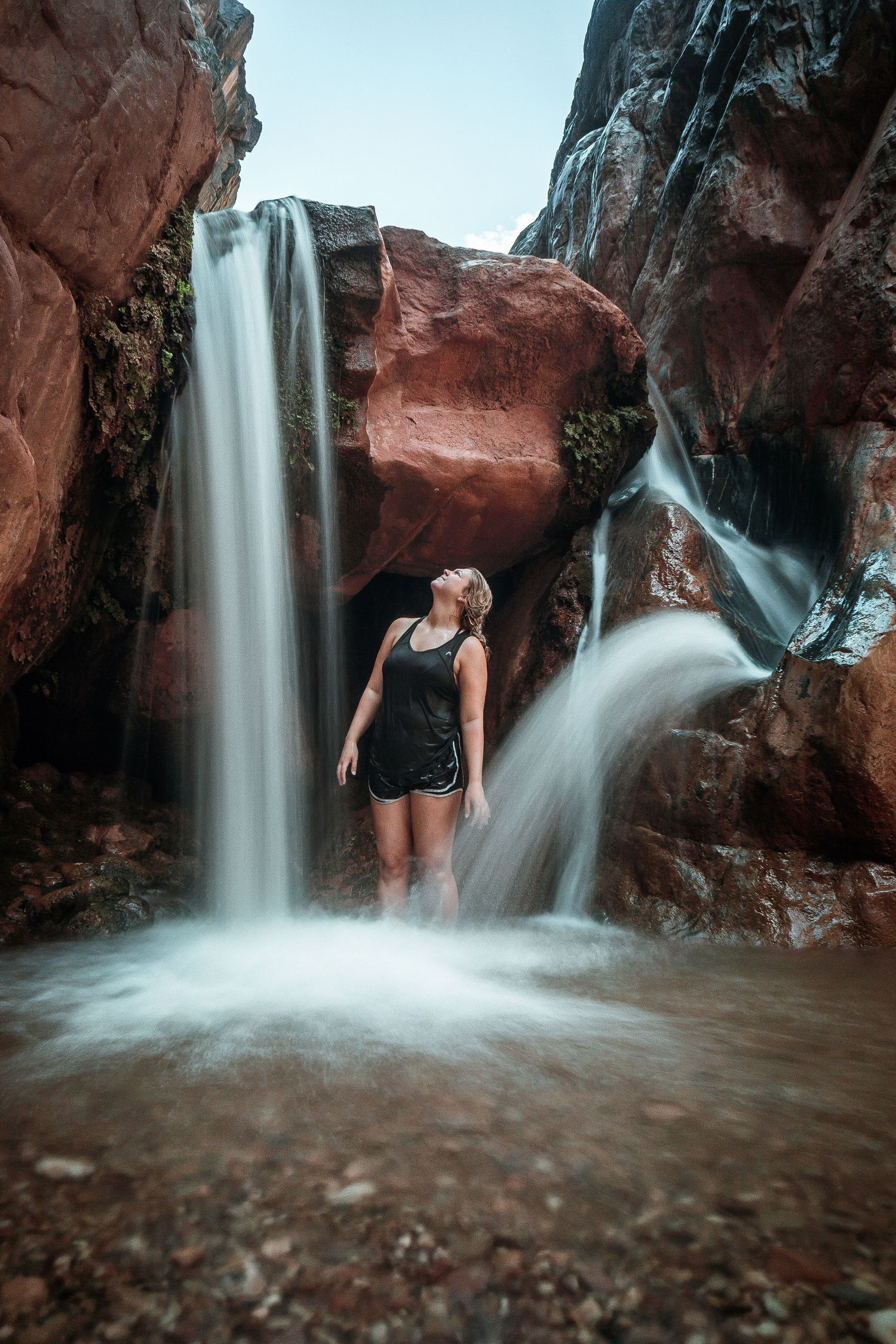 Woman standing between two waterfalls in a red rock canyon.