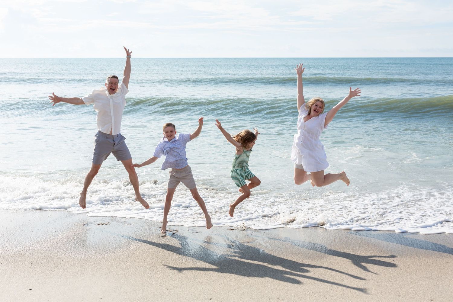 Family of four jumping joyfully on beach with ocean waves in background.