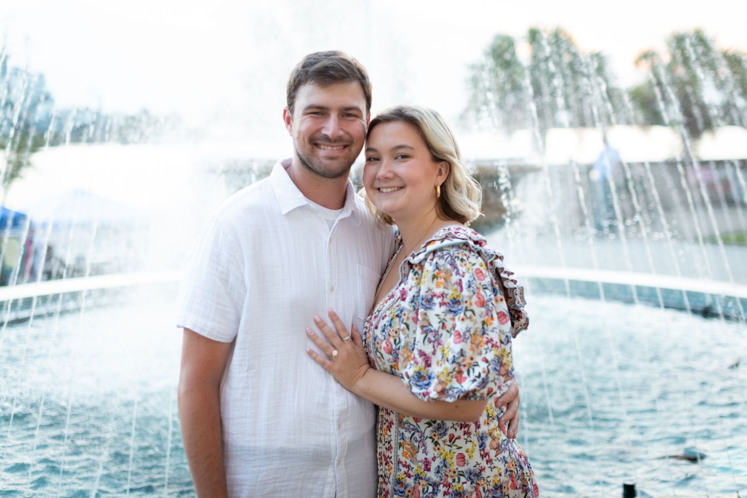 A couple poses together in front of a cascading water fountain on a sunny summer day.