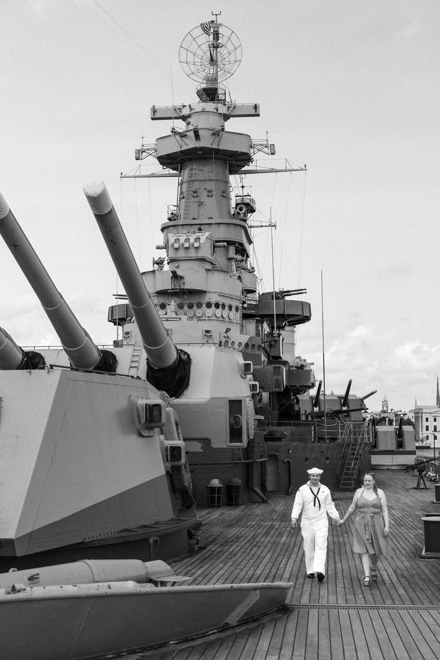 Historic black and white photos show sailors on the deck of a World War II battleship with large naval gun turrets.
