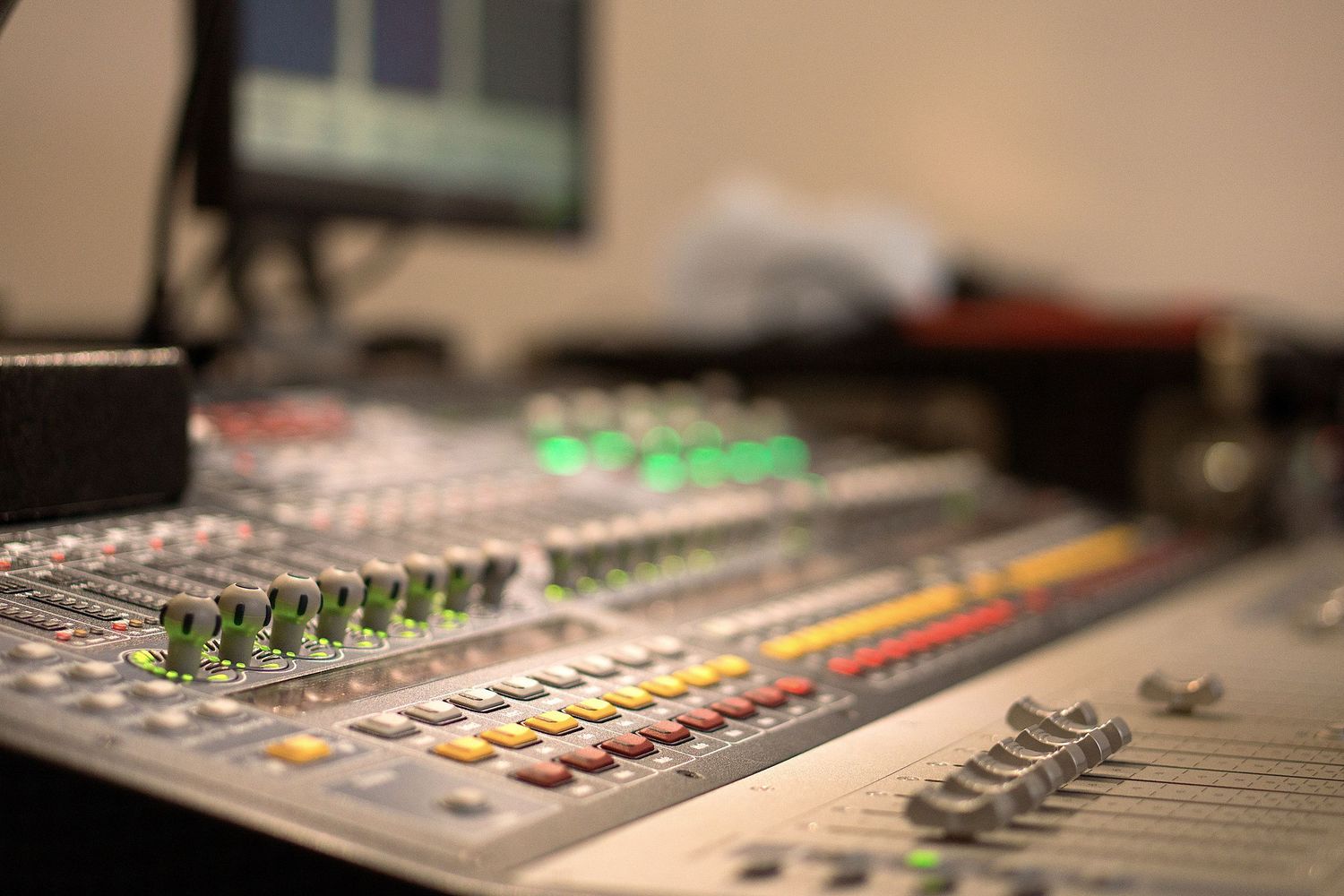 Professional audio mixing console with illuminated faders and control buttons in a recording studio setting.