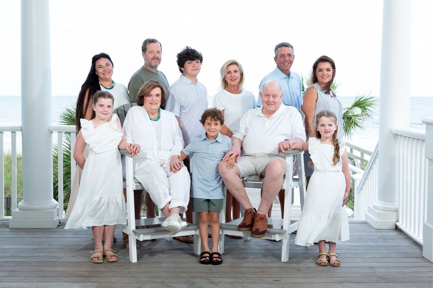 A group of people dressed in white and light colored clothing pose together on a beach boardwalk.