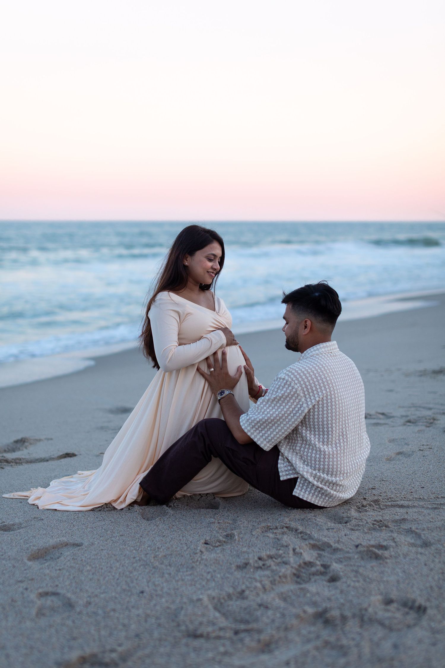 A couple sits together on a sandy beach at sunset sharing a romantic moment by the ocean waves.