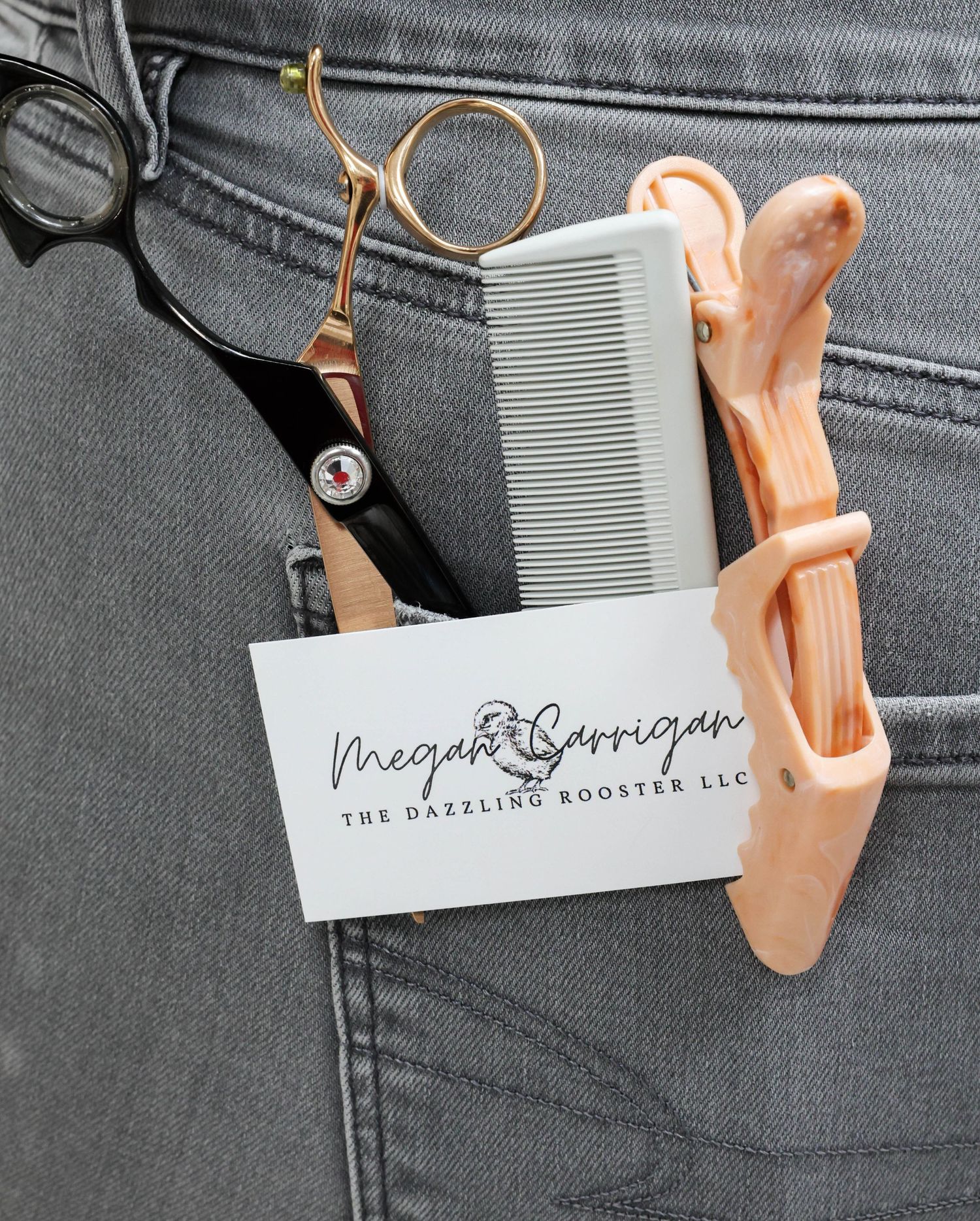 Hairstylist tools including scissors, comb, and clips in a jeans pocket with Megan Carrigan The Dazzling Rooster LLC business card.