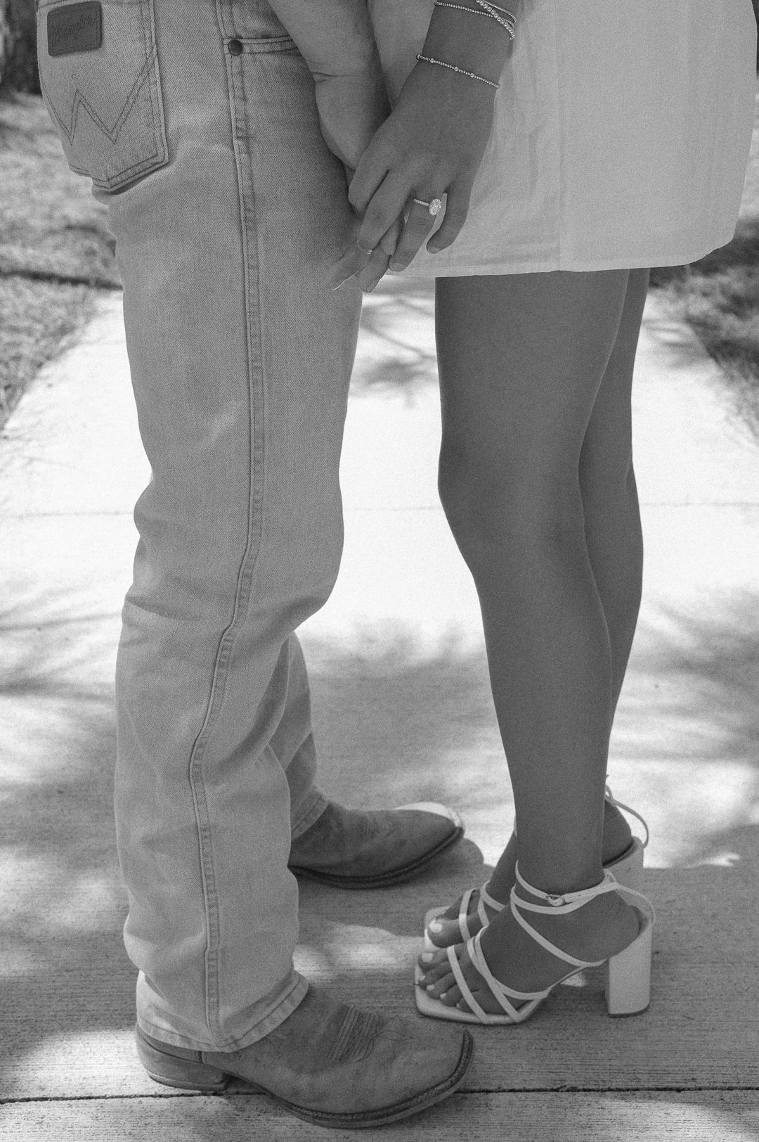 Black and white close-up of couple holding hands, wearing cowboy boots and heels.
