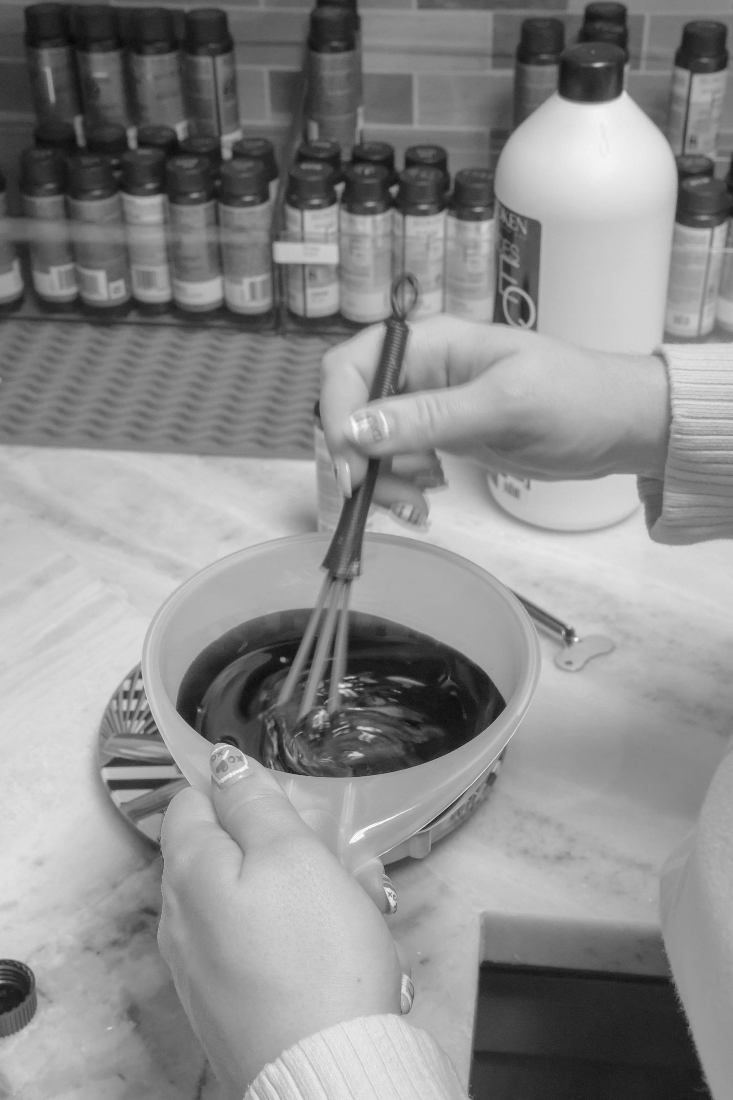 Black and white photo of hands mixing dark hair color in a bowl with a whisk at a salon.