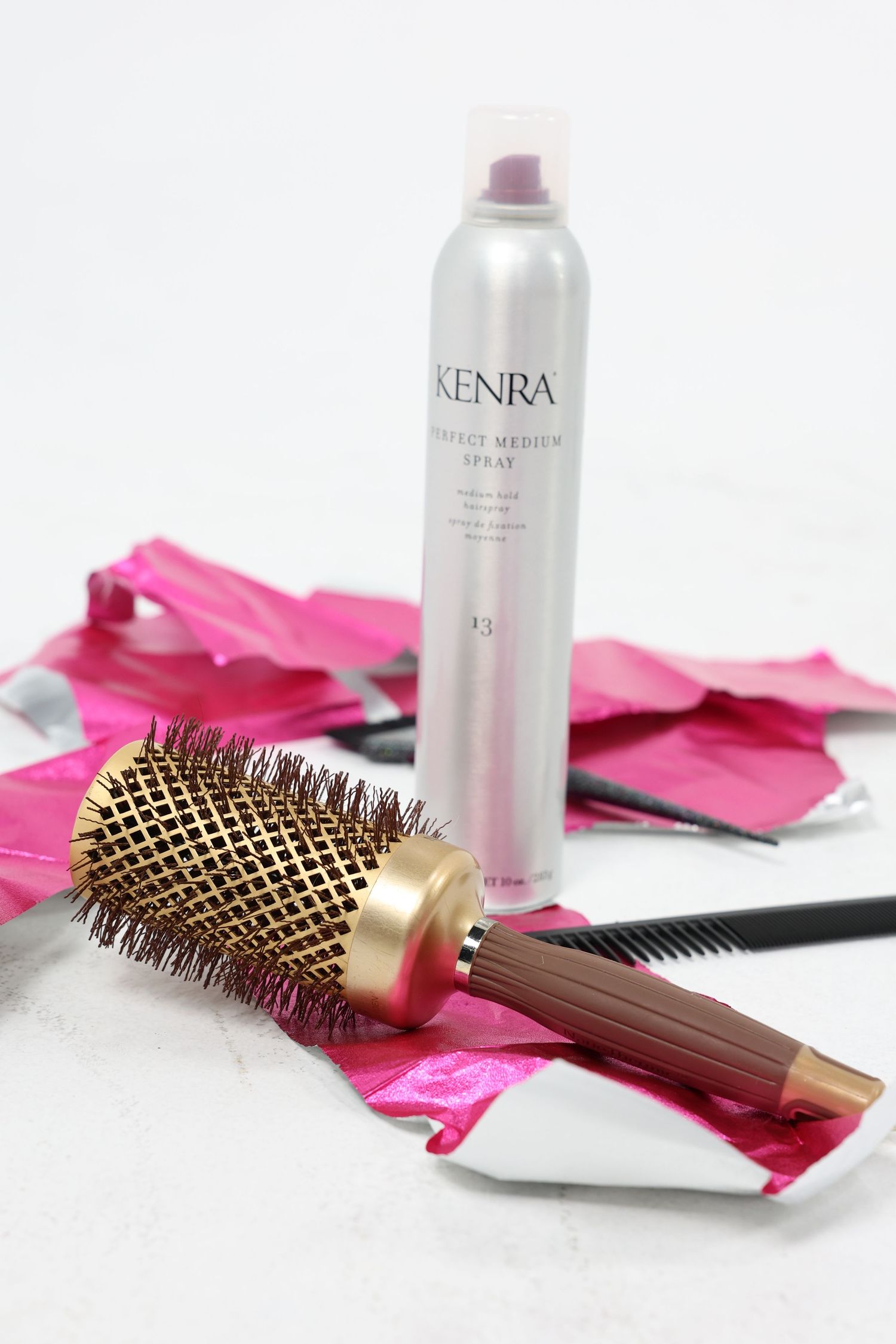 Kenra Perfect Medium Spray 13 with round brush and pink foils on white surface.