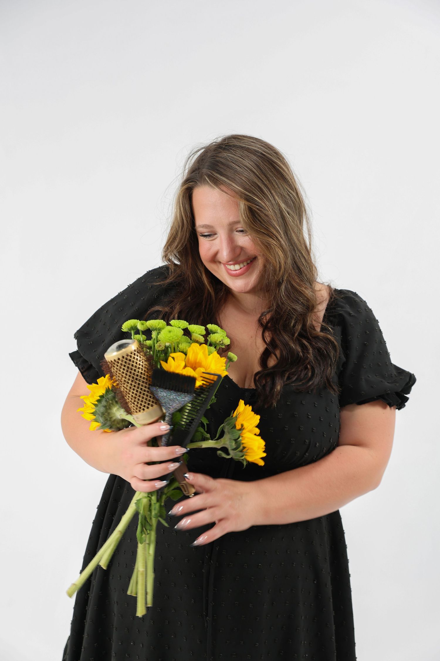Smiling woman in black dress holding a bouquet of sunflowers and green flowers.