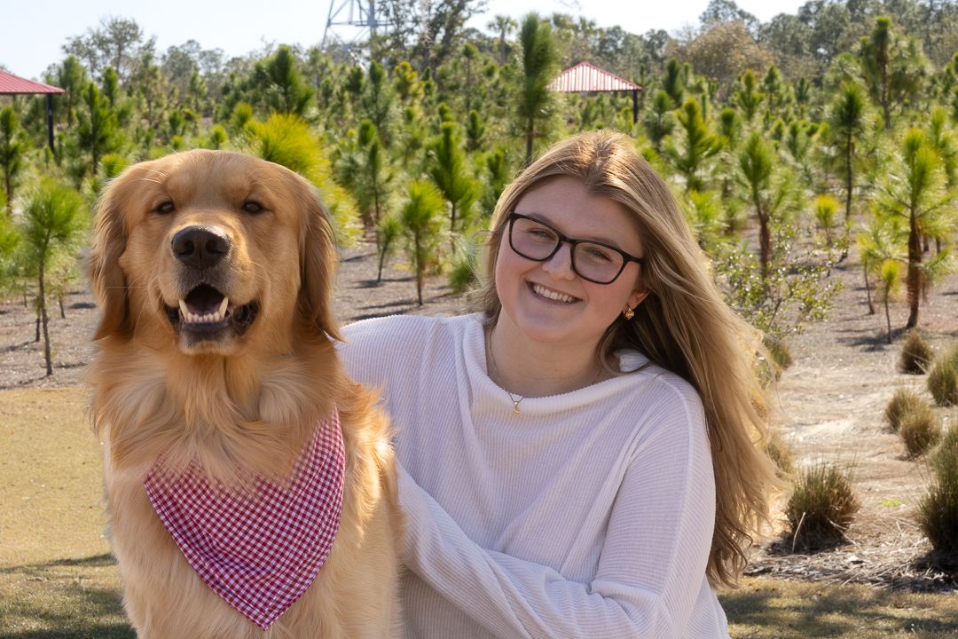 Smiling teenage girl posing with her Golden Retriever dog wearing a pink bandana outdoors.