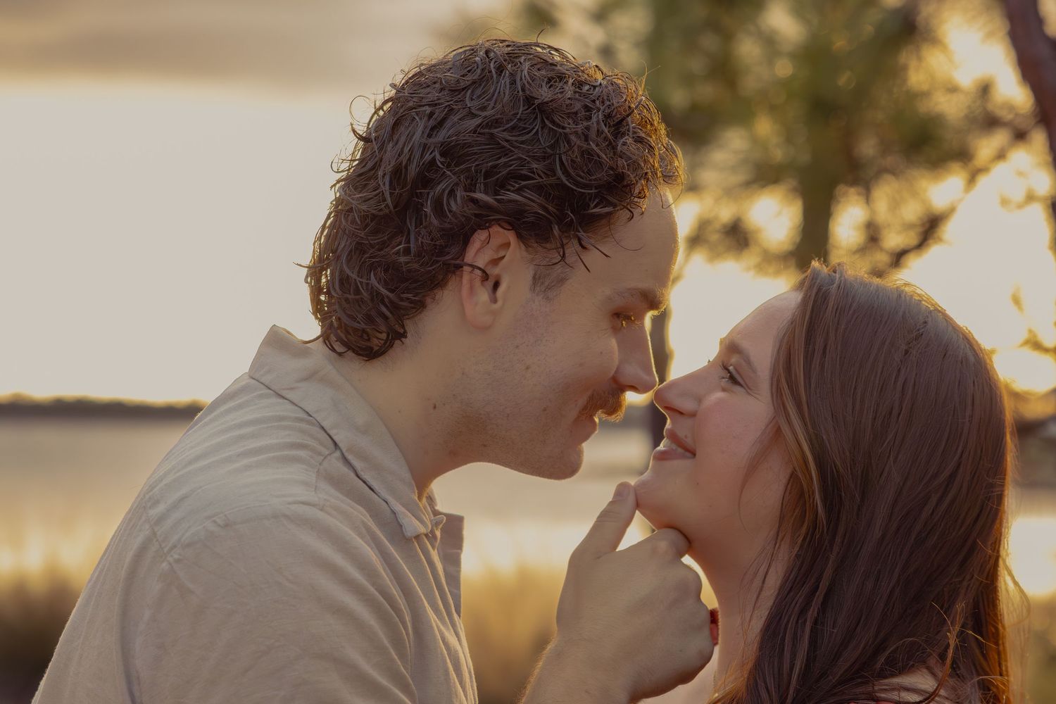 Close-up of smiling couple about to kiss at warm golden sunset outdoors.